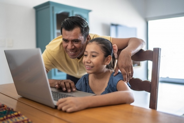 Mexican father helping daughter on laptop digital literacy Getty
