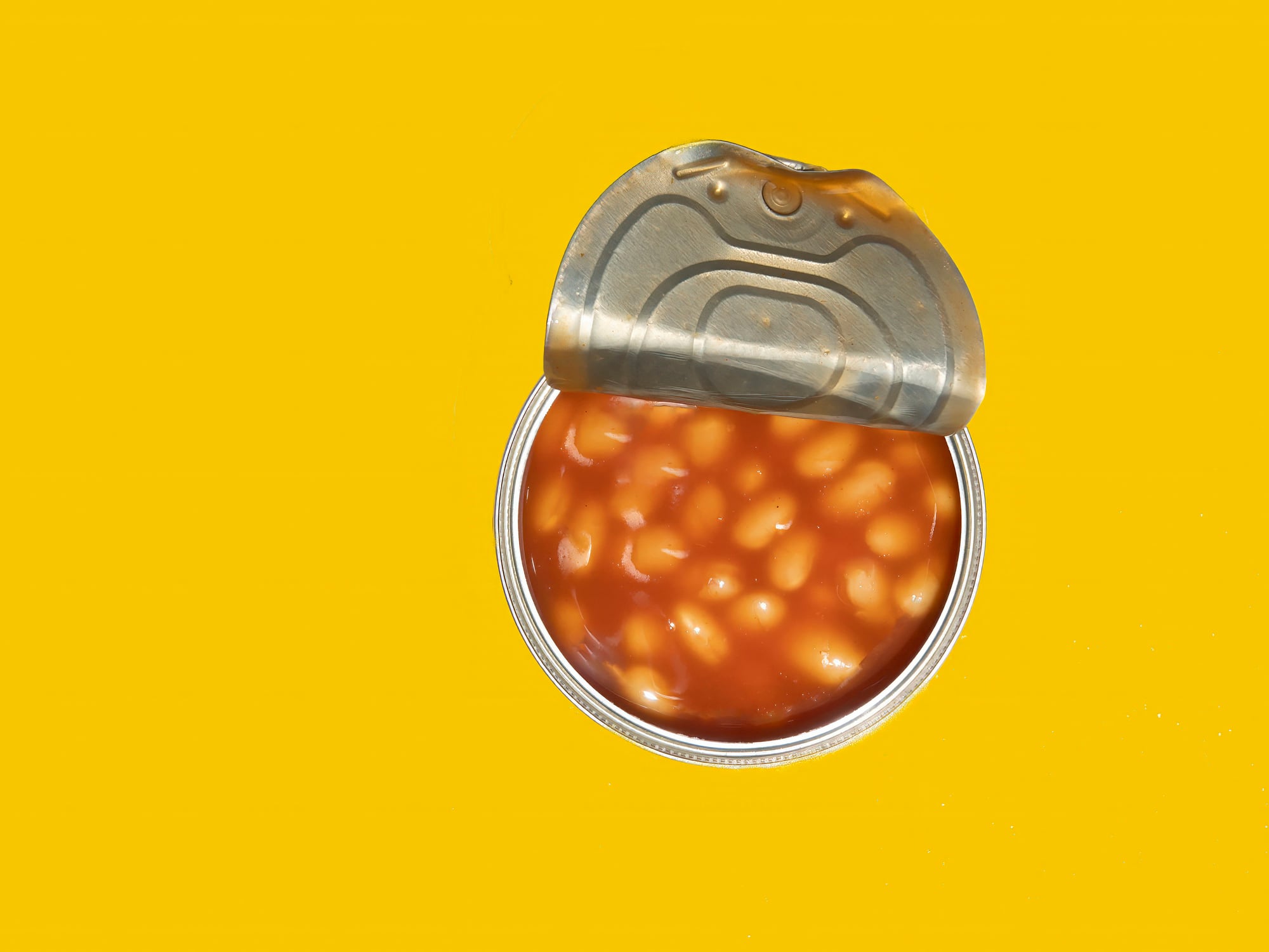 Open can of Baked Beans on a yellow background