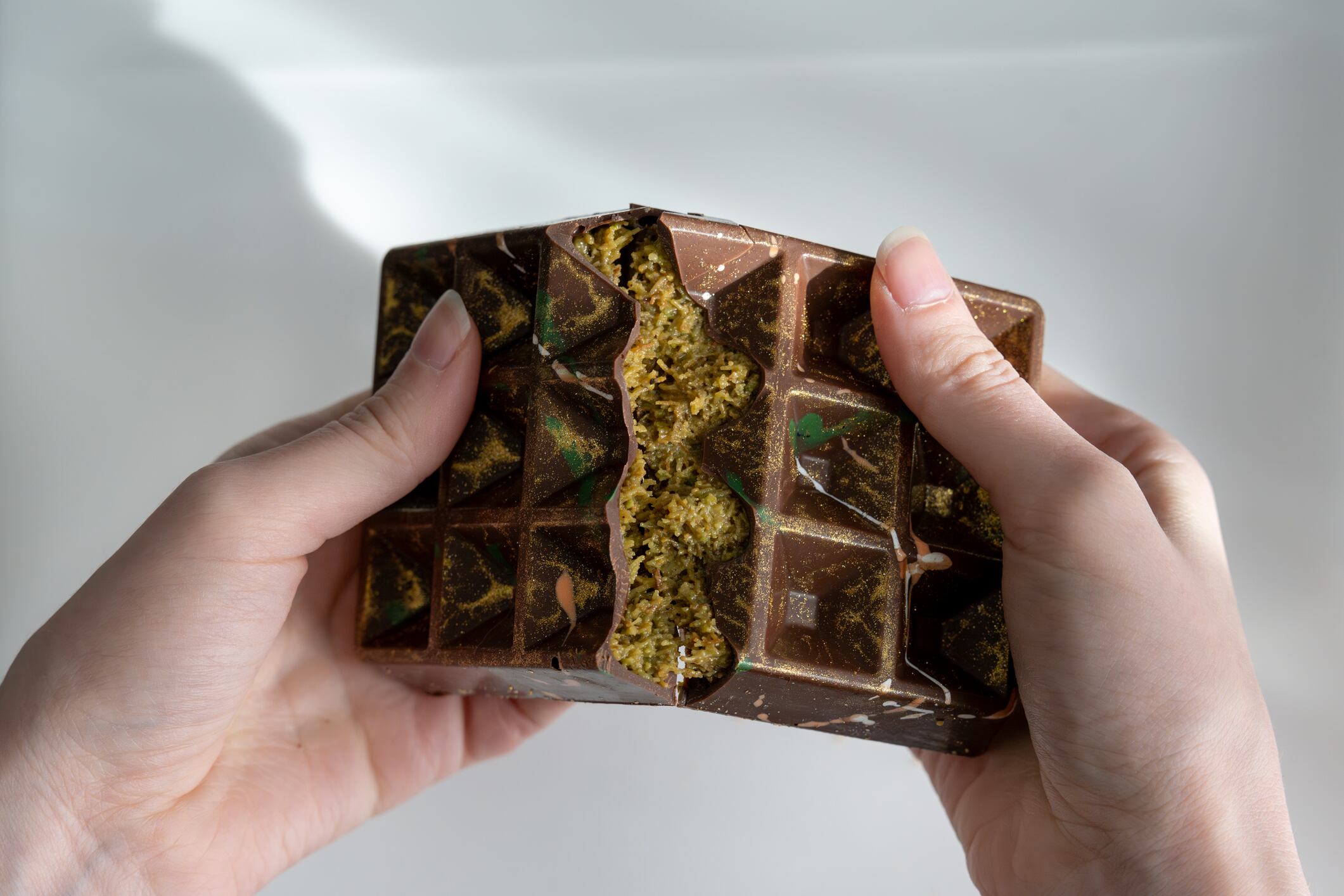 Dubai chocolate, viral chocolate , trends, homemade chocolate with pistachio, tahini and kadaif, chocolate broken in woman's hands,. High quality photo