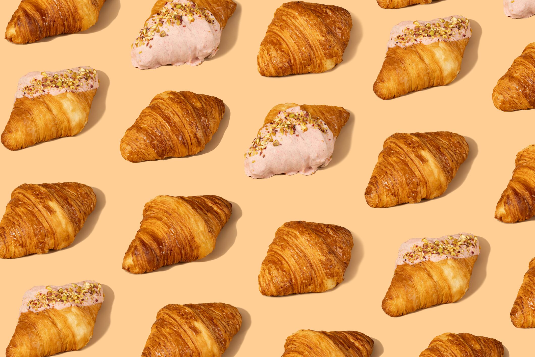 Pattern of Fresh croissant against a pastel peach background, showcasing their flaky layers and golden crusts. Perfect for bakery promotions and breakfast themes.