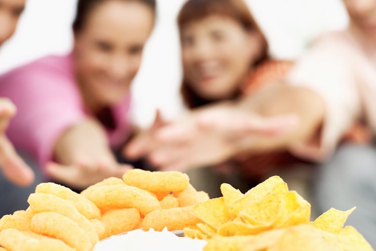 Close up of dishes of assorted crisps and dip on a table and two young couples in the background reaching for snacks Getty Images Stockbyte