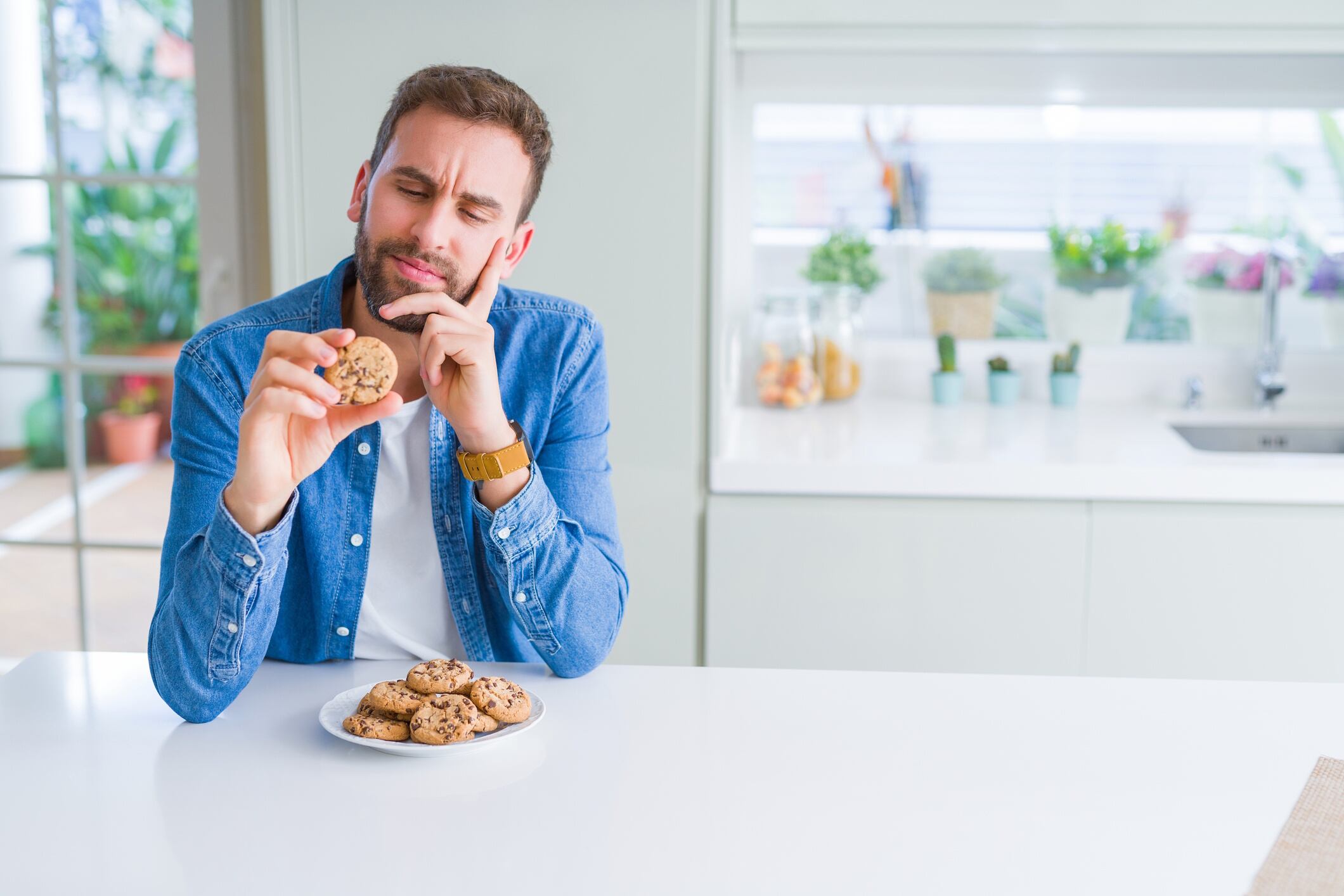 Handsome man eating chocolate chips cookies serious face thinking about question, very confused idea AaronAmat GettyImages