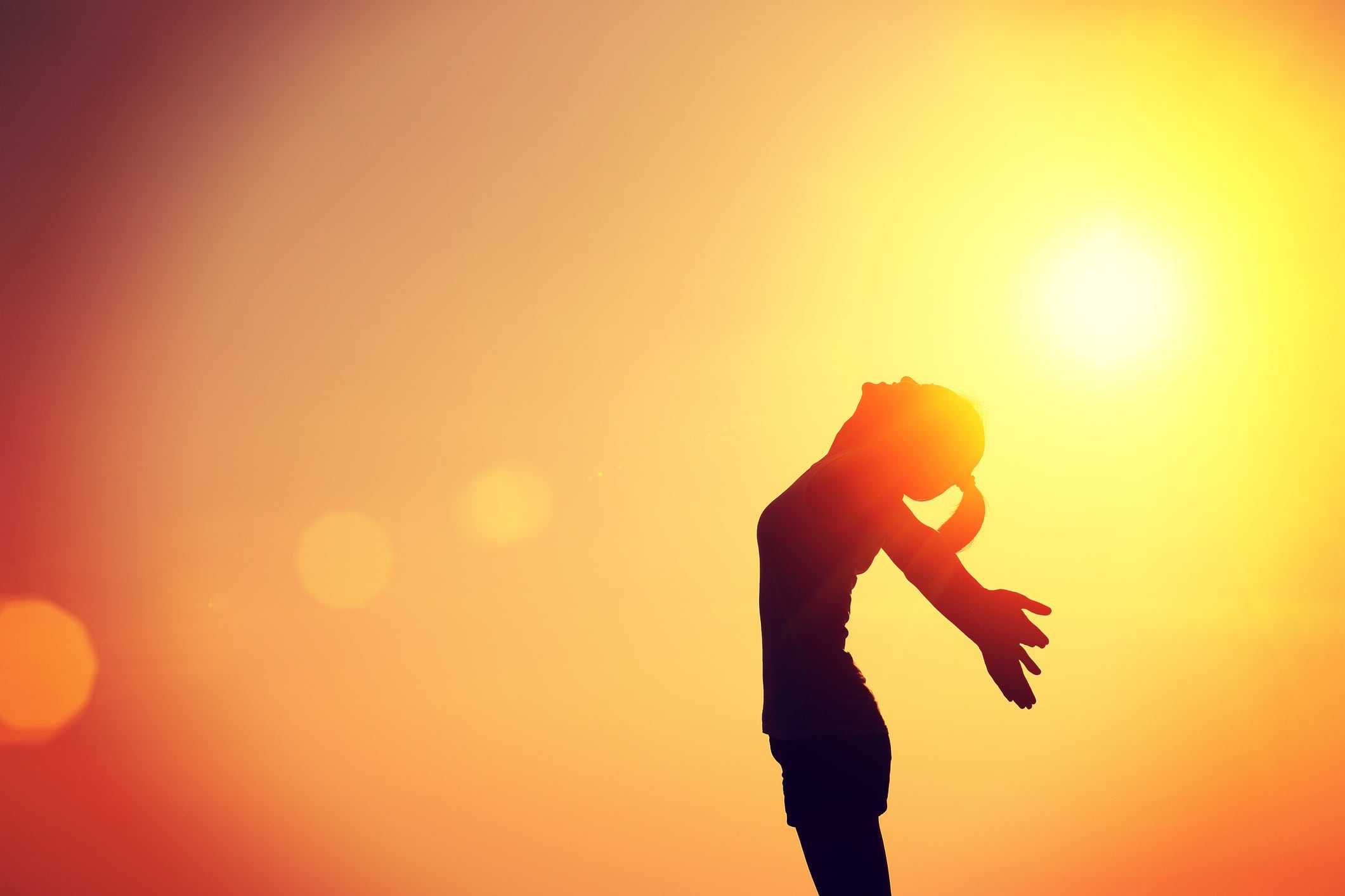 Woman in silhouette - arms raised against the sun at sunset.