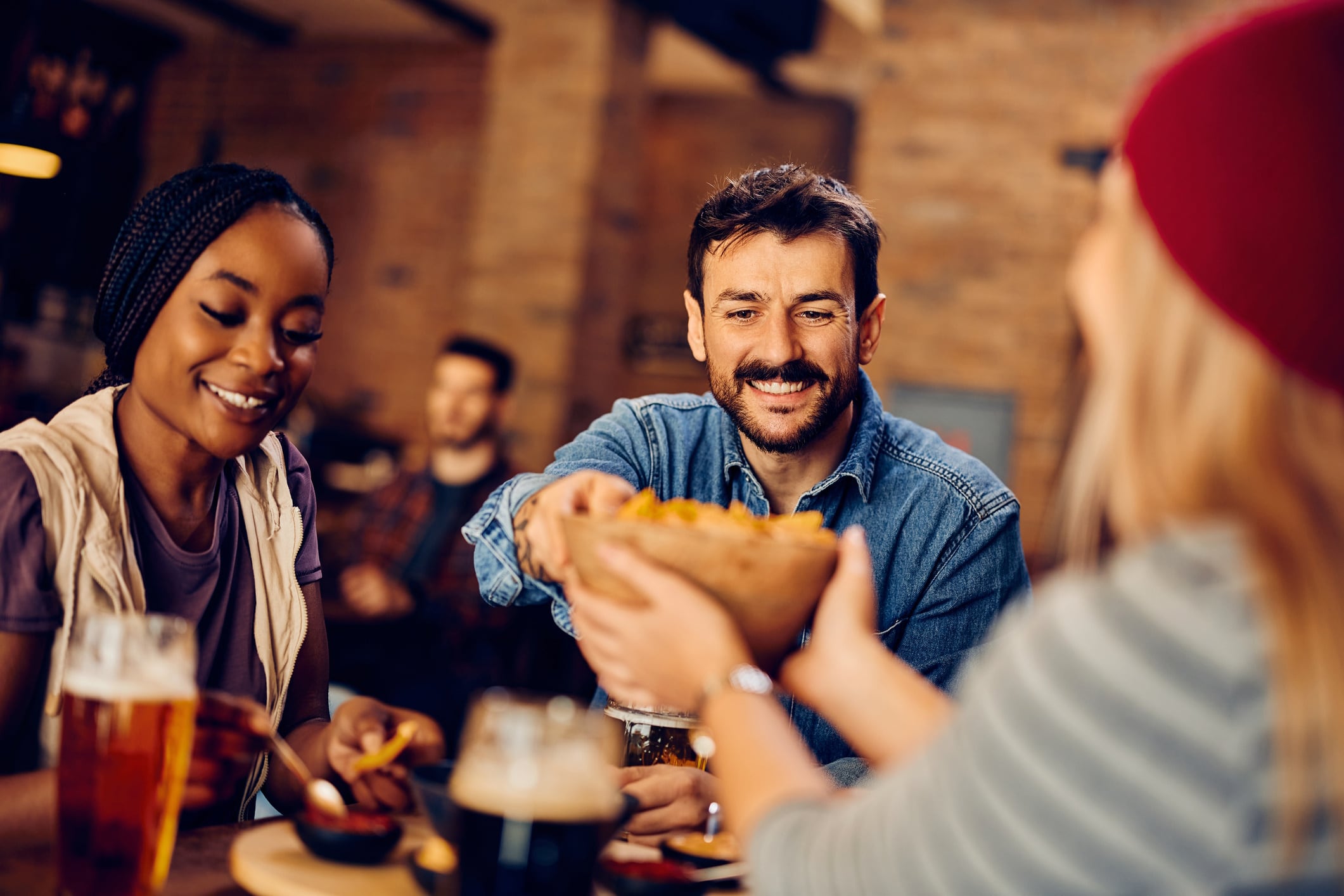 Happy man and his friends eating nacho chips and drinking beer while gathering in bar