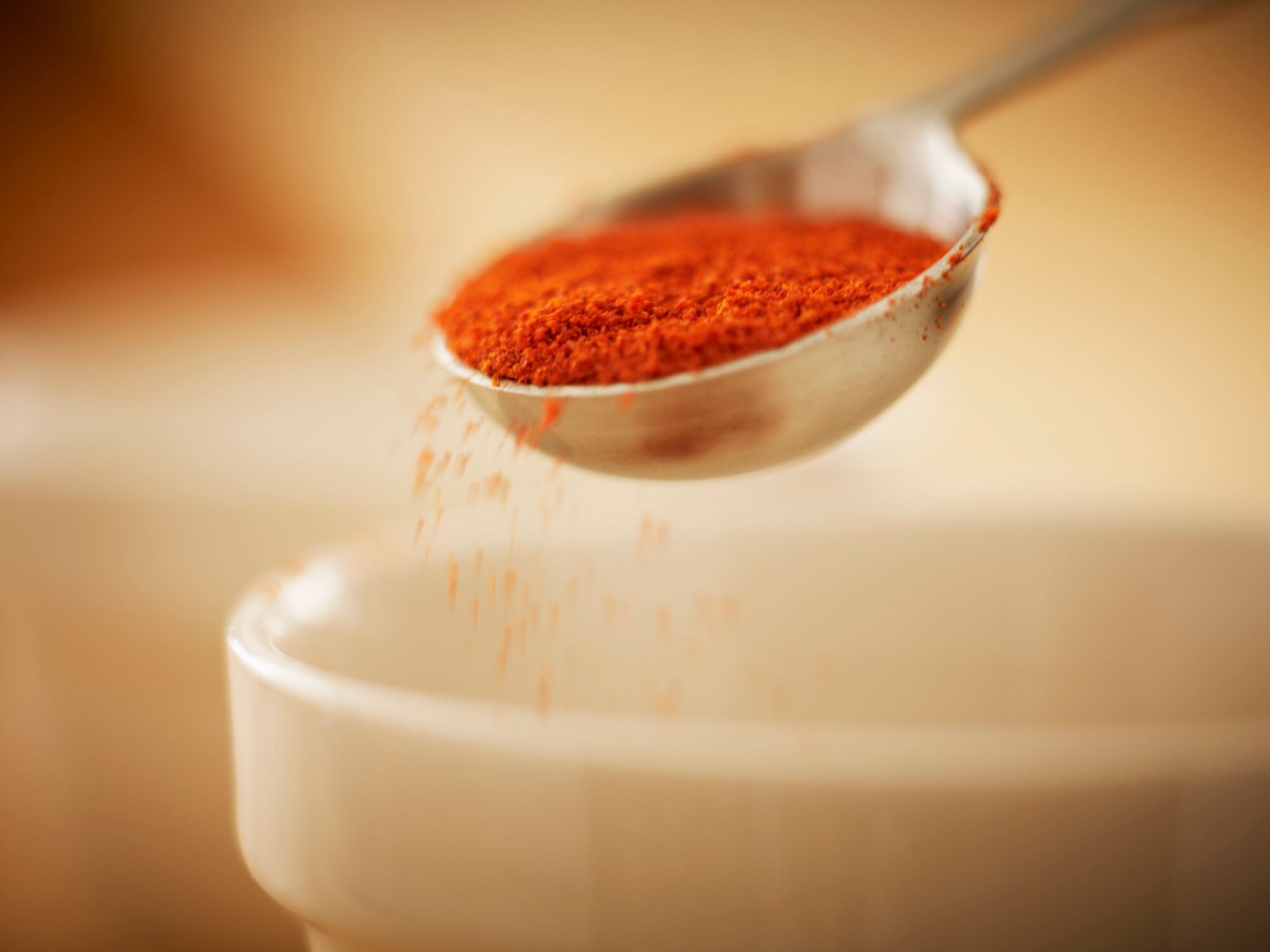 Close up of spice in measuring spoon sprinkling into bowl
