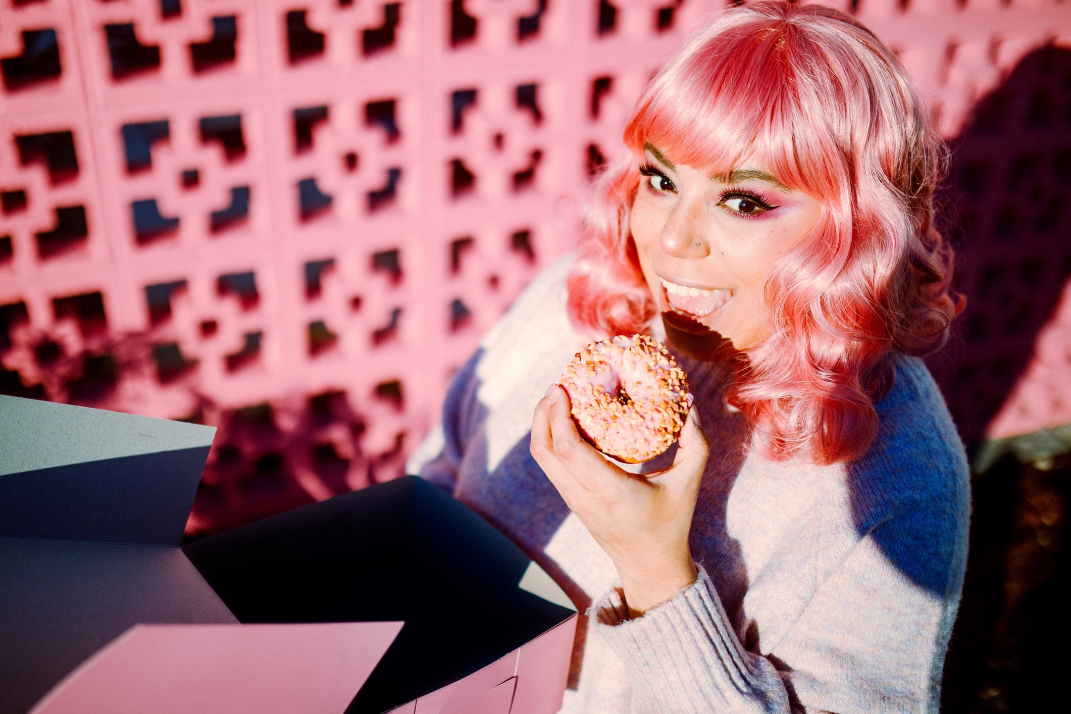 Pink haired lady eating a pink doughnut