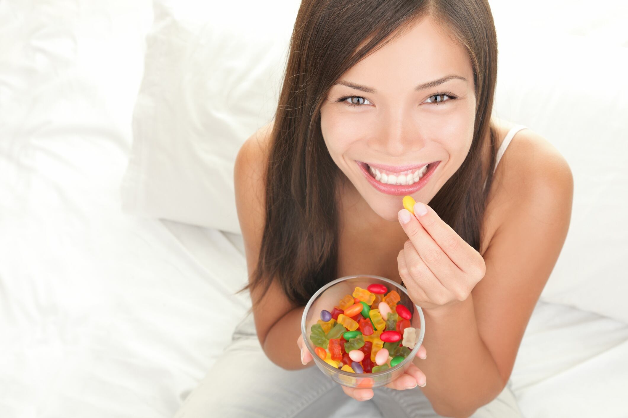 Woman eating gummies while sat on bed.