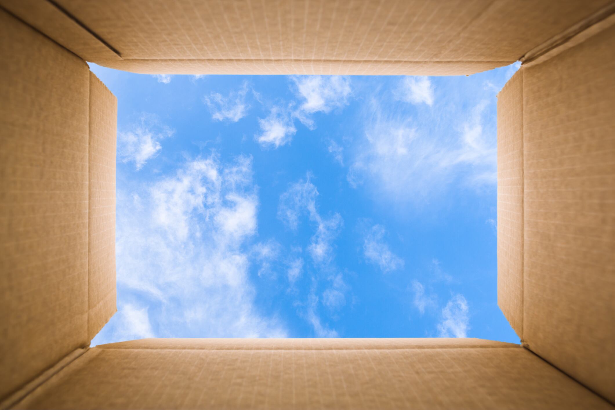 Image: Thinking outside the box concept: Blu sky with some white clouds viewed from inside of a cardboard box. The carton sides are aligned with the image sides and sky is framed in the center of the image.