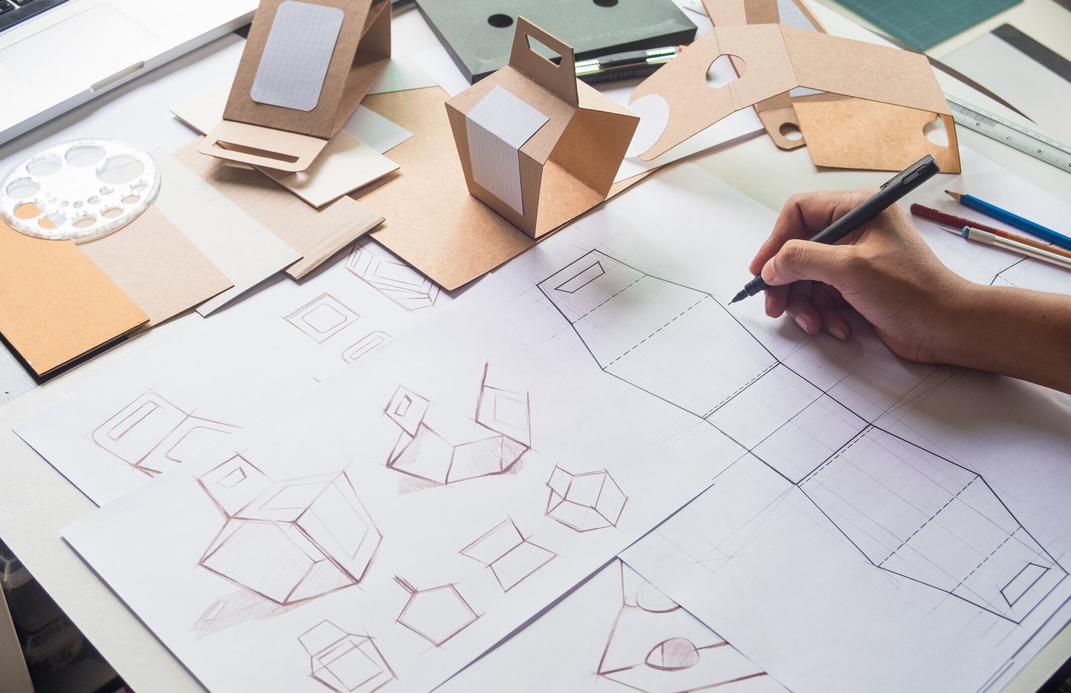 Person sketching packaging, with cardboard boxes above