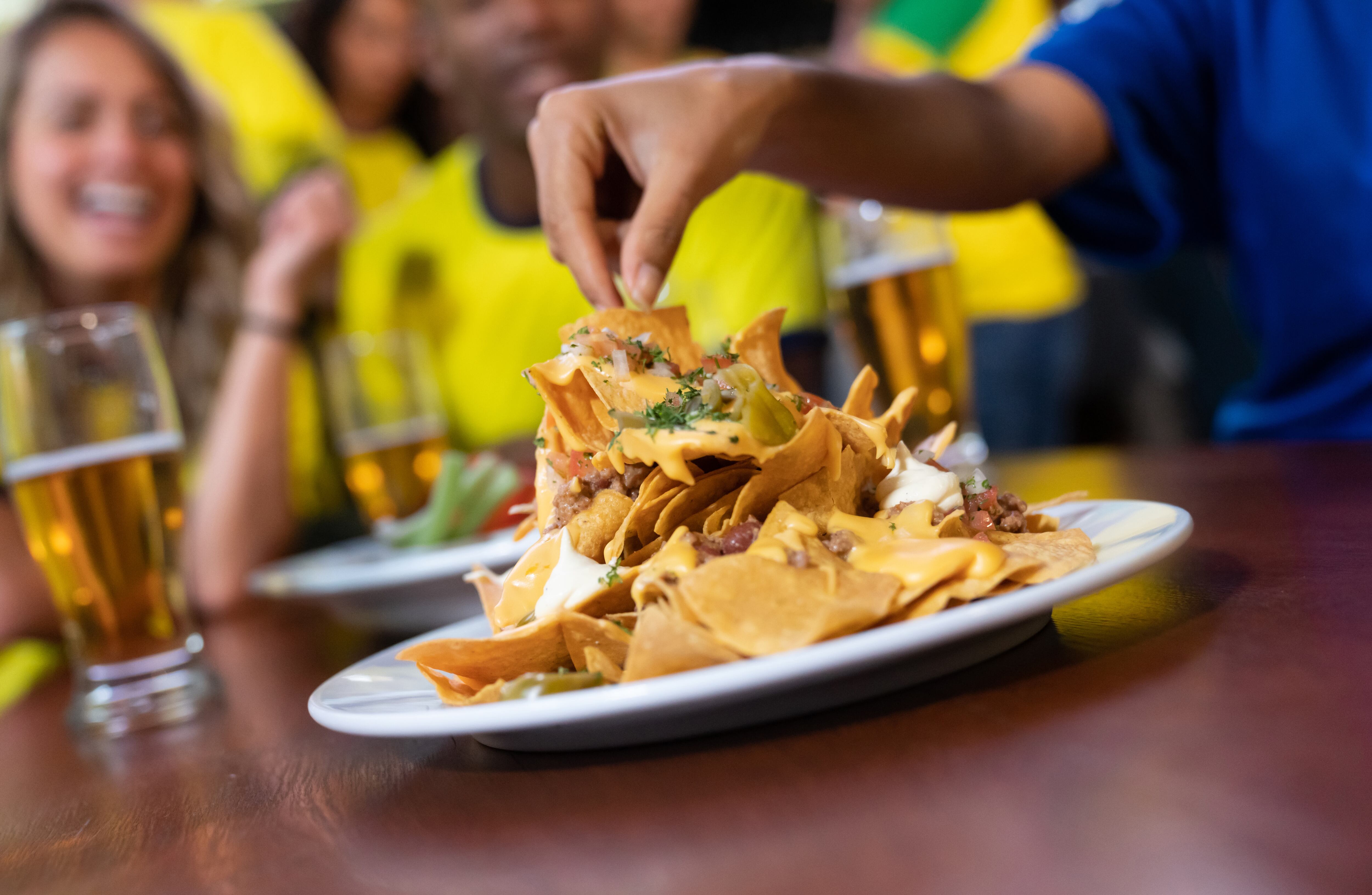 Close up on nachos at a sports bar while friends are watching a game