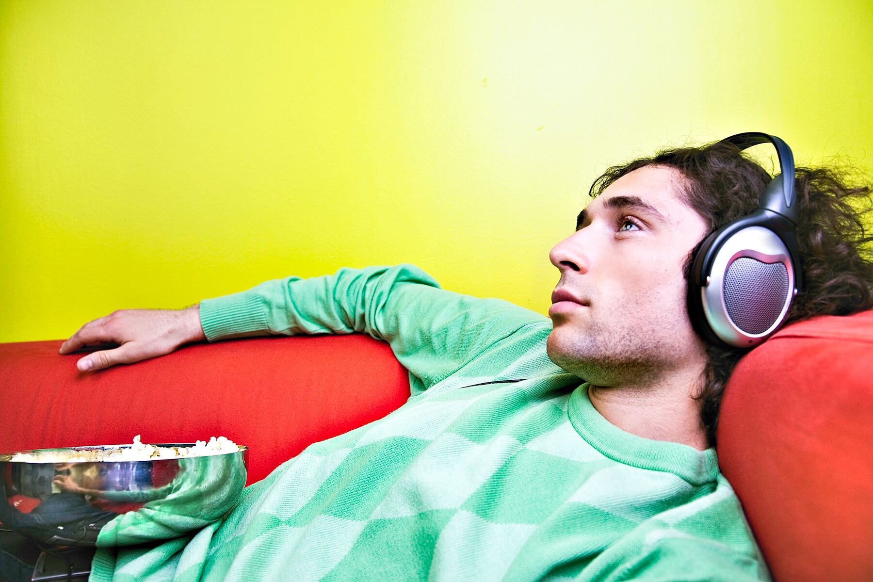 Young man listening to music on the couch with popcorn