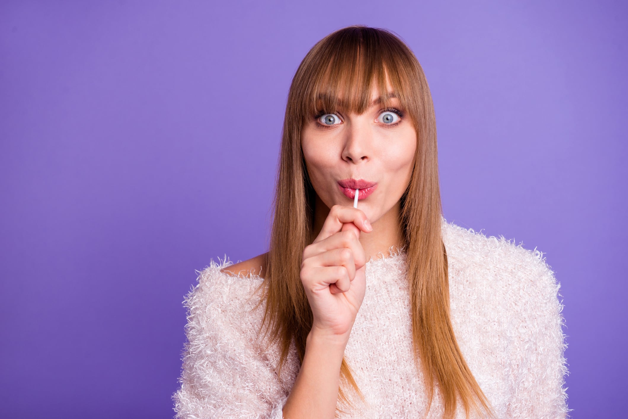 Portrait funny cute childish teen teenager carefree playful hold hand lolipop yellow astonished impressed think unexpected incredible stylish isolated purple background fashionable woolen pullover Deagreez GettyImages