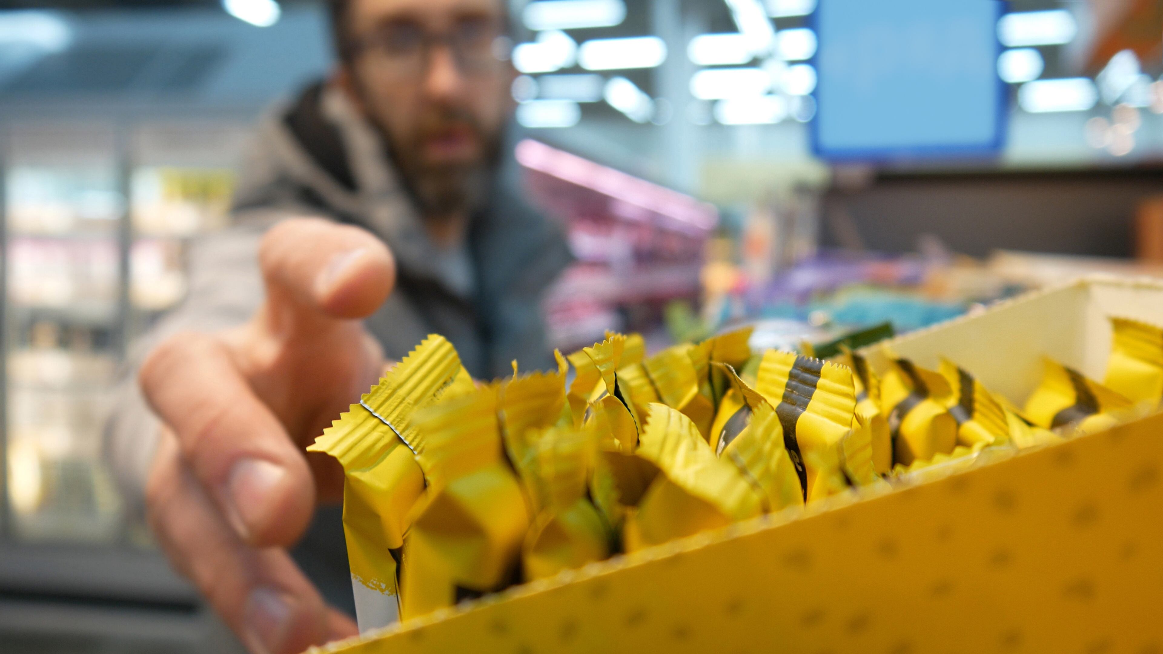 Close-up of many protein bars on the shelf of a supermarket and a male buyer reaching the hand to take one