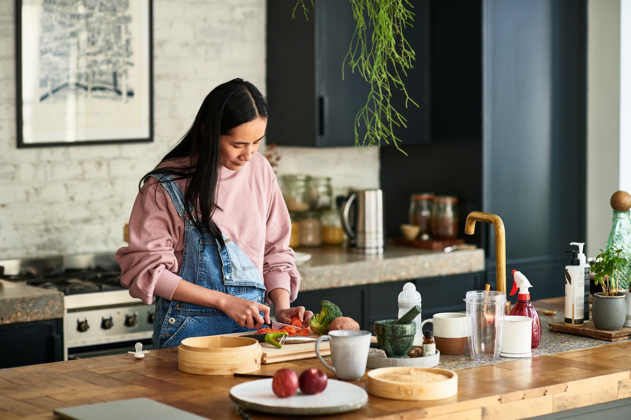 Woman chopping ingredients for meal, standing behind kitchen worktop.