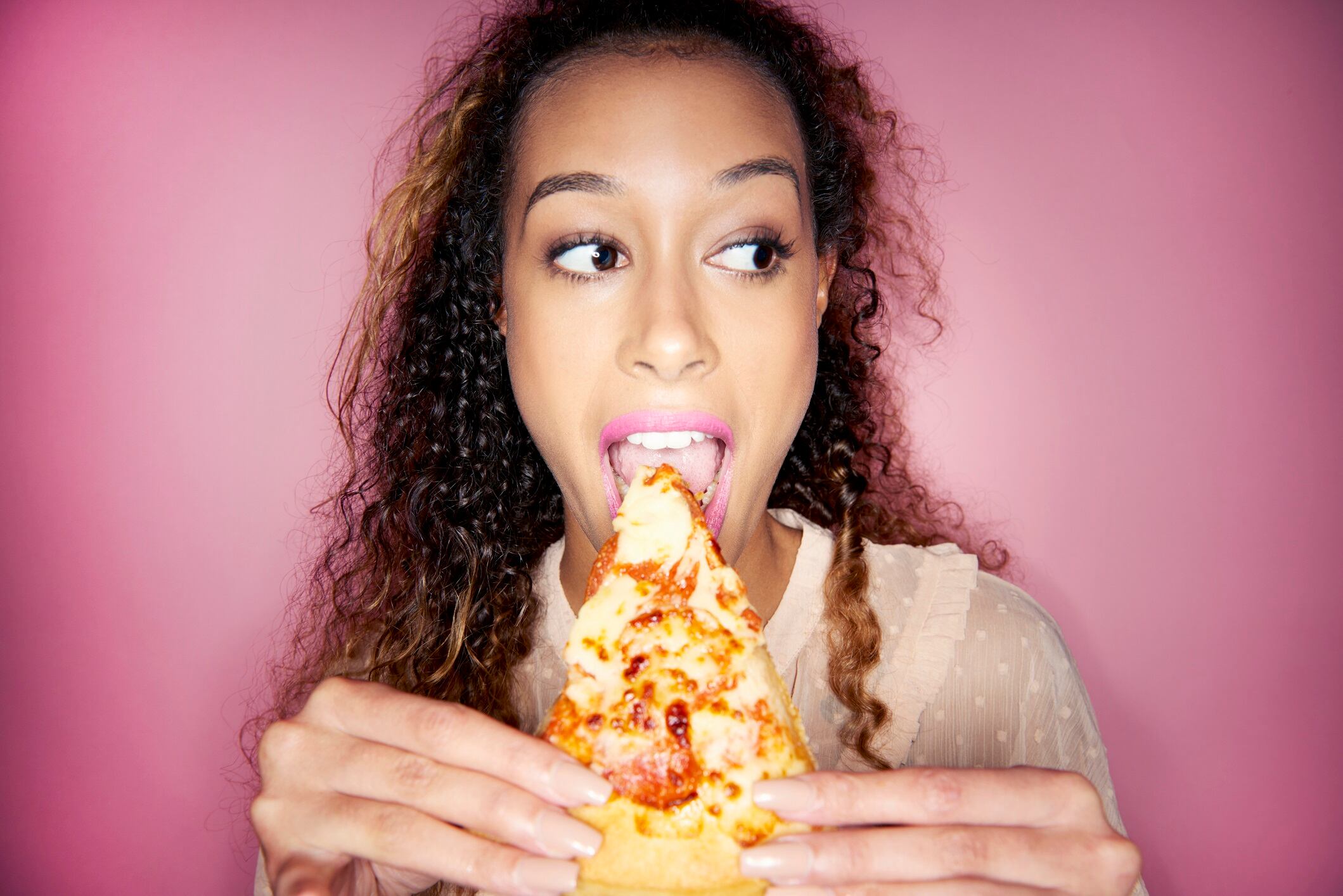 Woman eating pizza slice. Pink background.