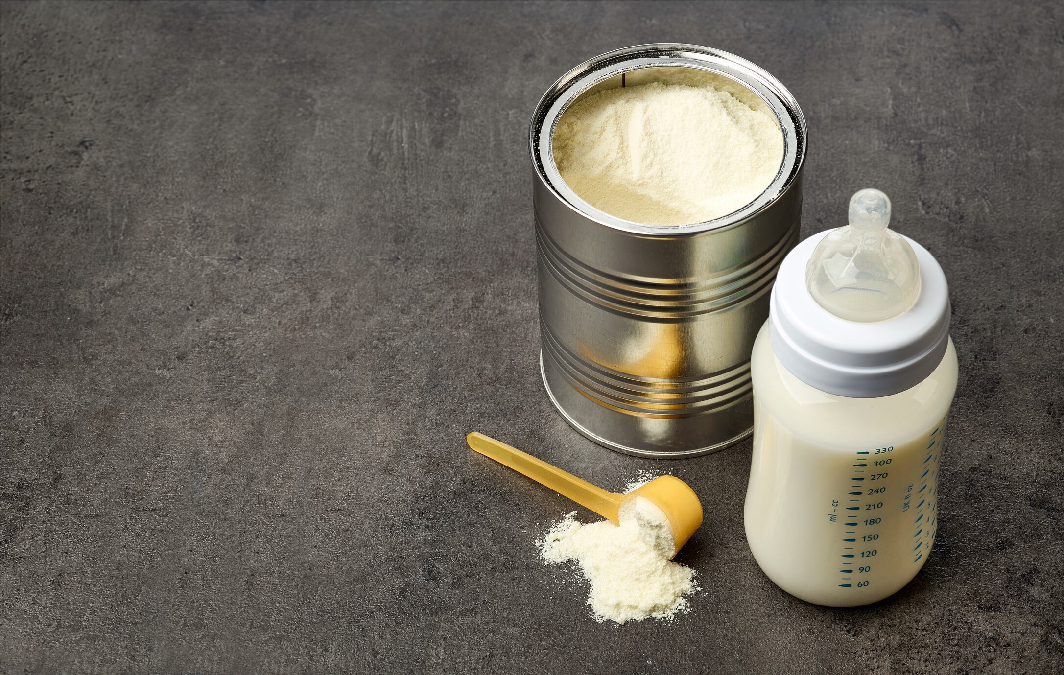 Baby bottle and milk powder on dark grey table