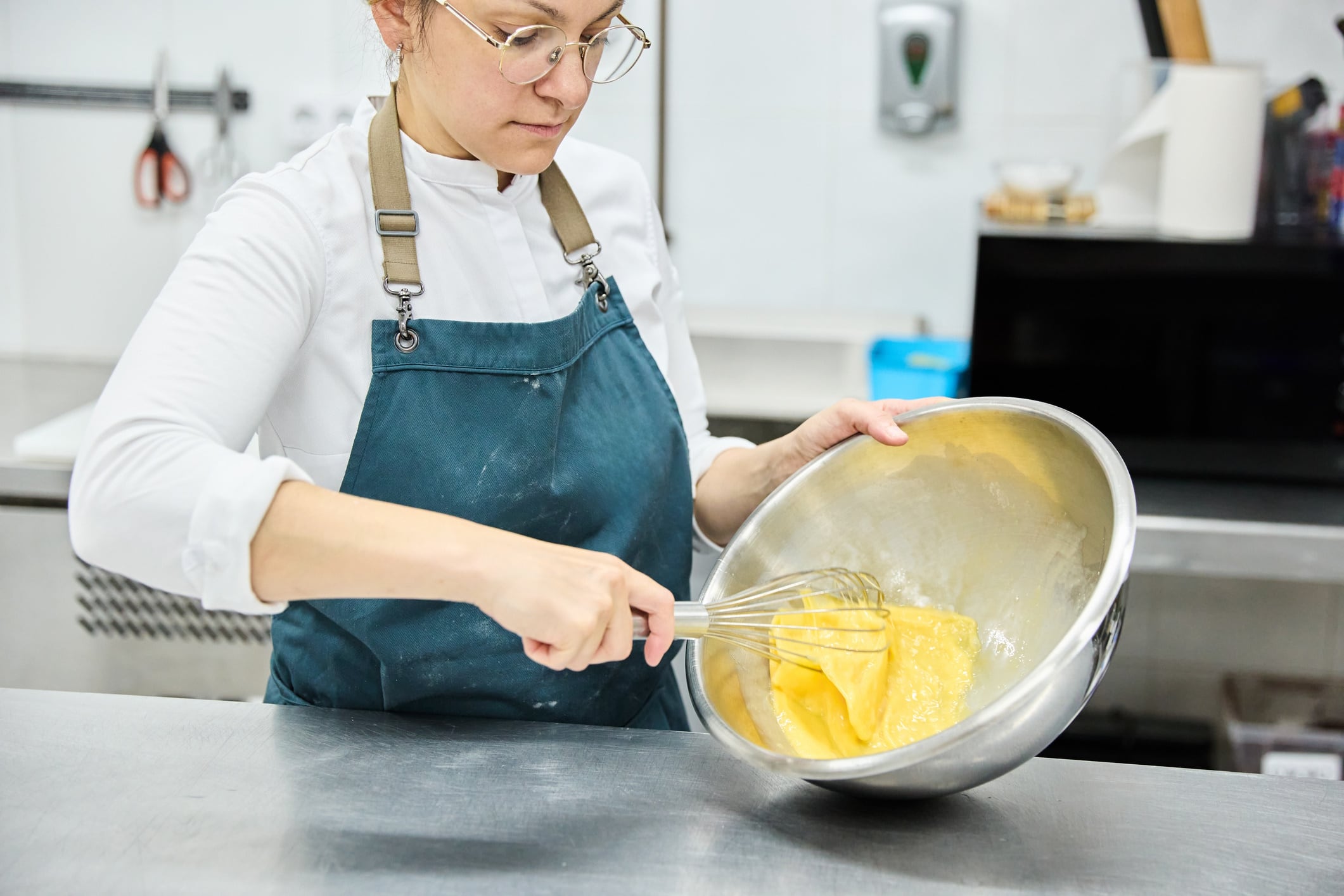 Young woman pastry chef beating eggs while preparing a delicious cake in the kitchen of a pastry shop