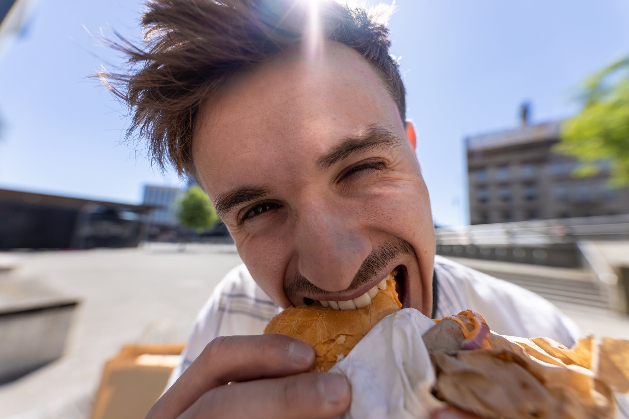 Extreme close-up wide-angle shot of a young adult male sitting in a city centre pedestrianised area in Newcastle-upon-Tyne, North East England. He is taking a bite from a sandwich. SolStock GettyImages