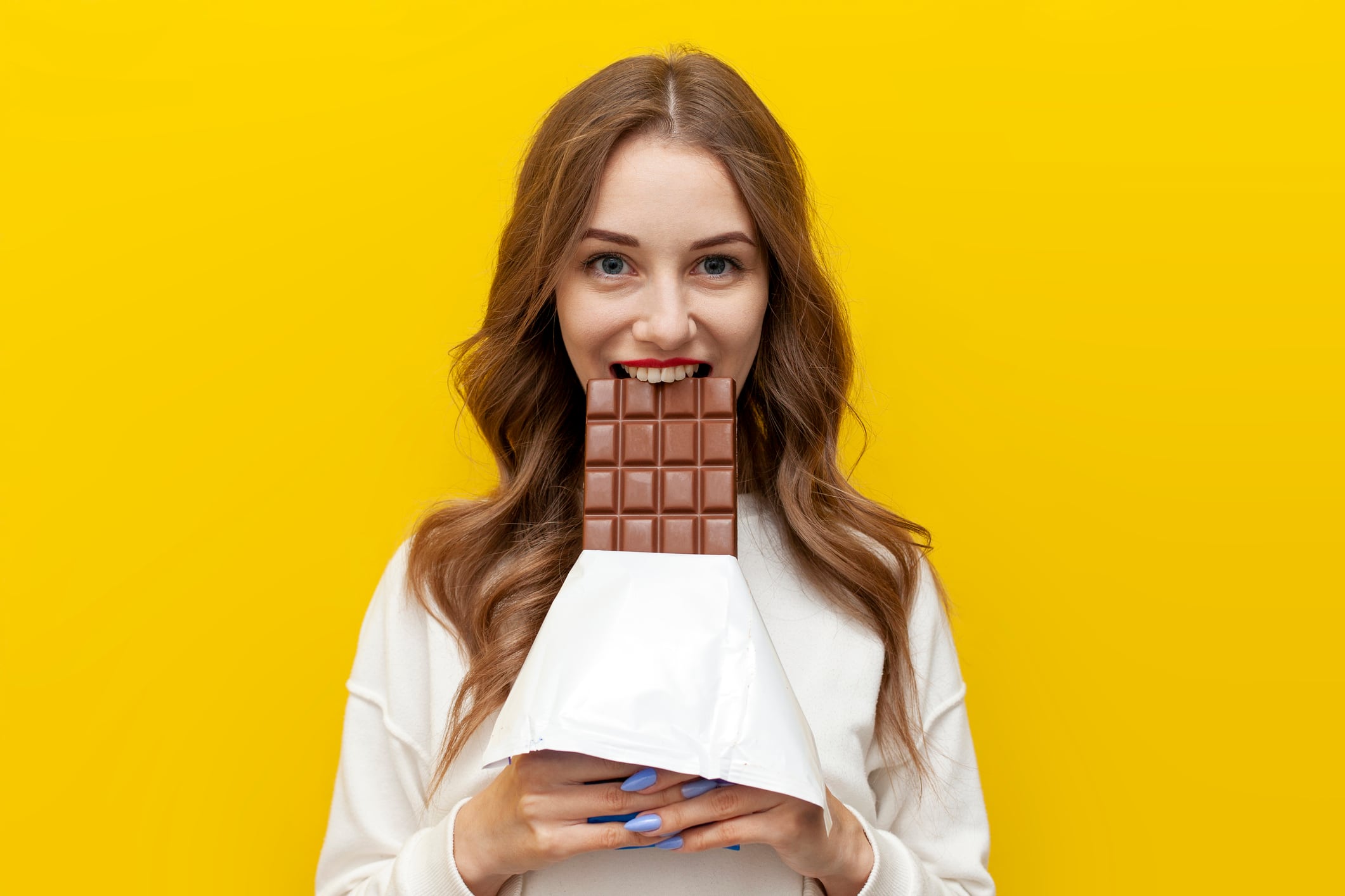 Woman eating large chocolate bar. Yellow background.