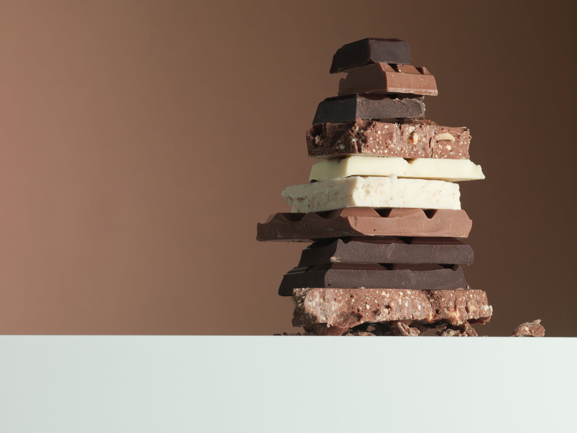 A pile of white, dark and nutty chocolate on a brown background.