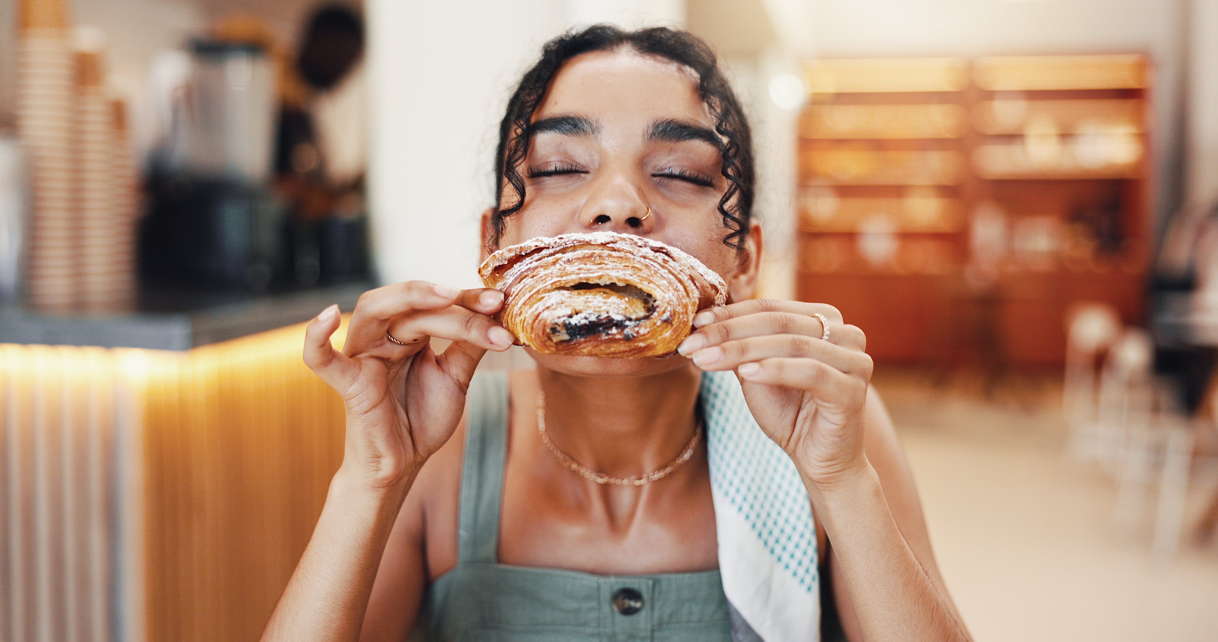 Cafe, happy and woman pastry eating for breakfast with snack, meal and hungry with craving Jacob Wackerhausen GettyImages