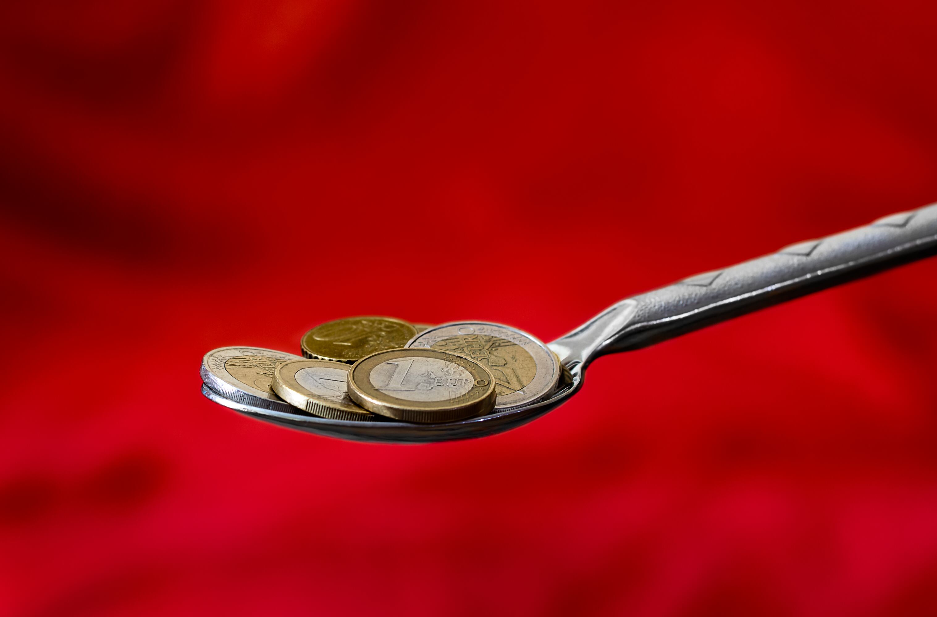 Spoon full of euro coins on a red background