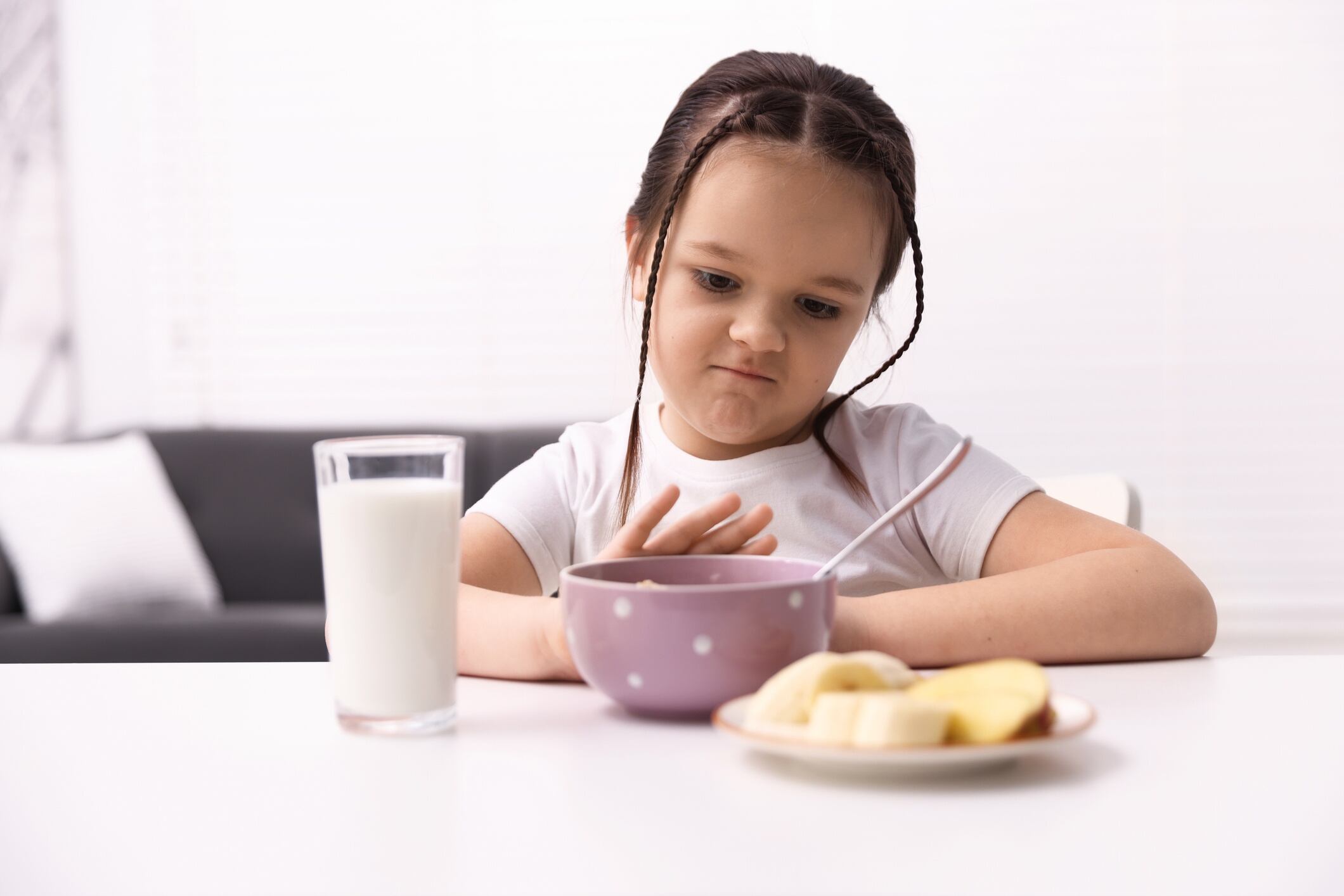 Unhappy little girl refusing to porridge, milk and fruits at white table indoors Olga Yastremska GettyImages