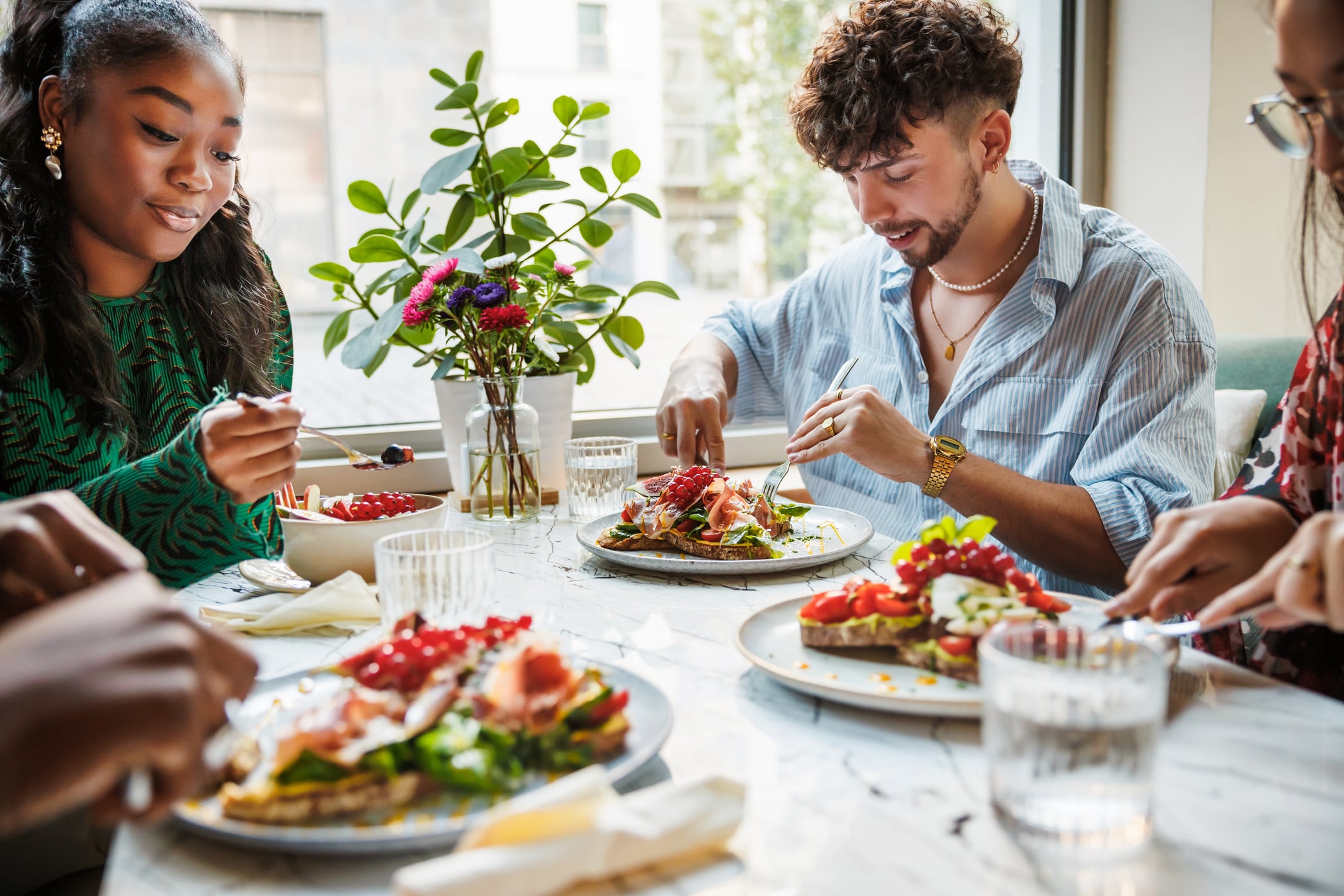 Health app Zoe launches UPF risk scale. Image: A lively brunch scene with a close-knit group of friends enjoying a healthy and vibrant meal together in a sunlit, plant-filled city cafe.