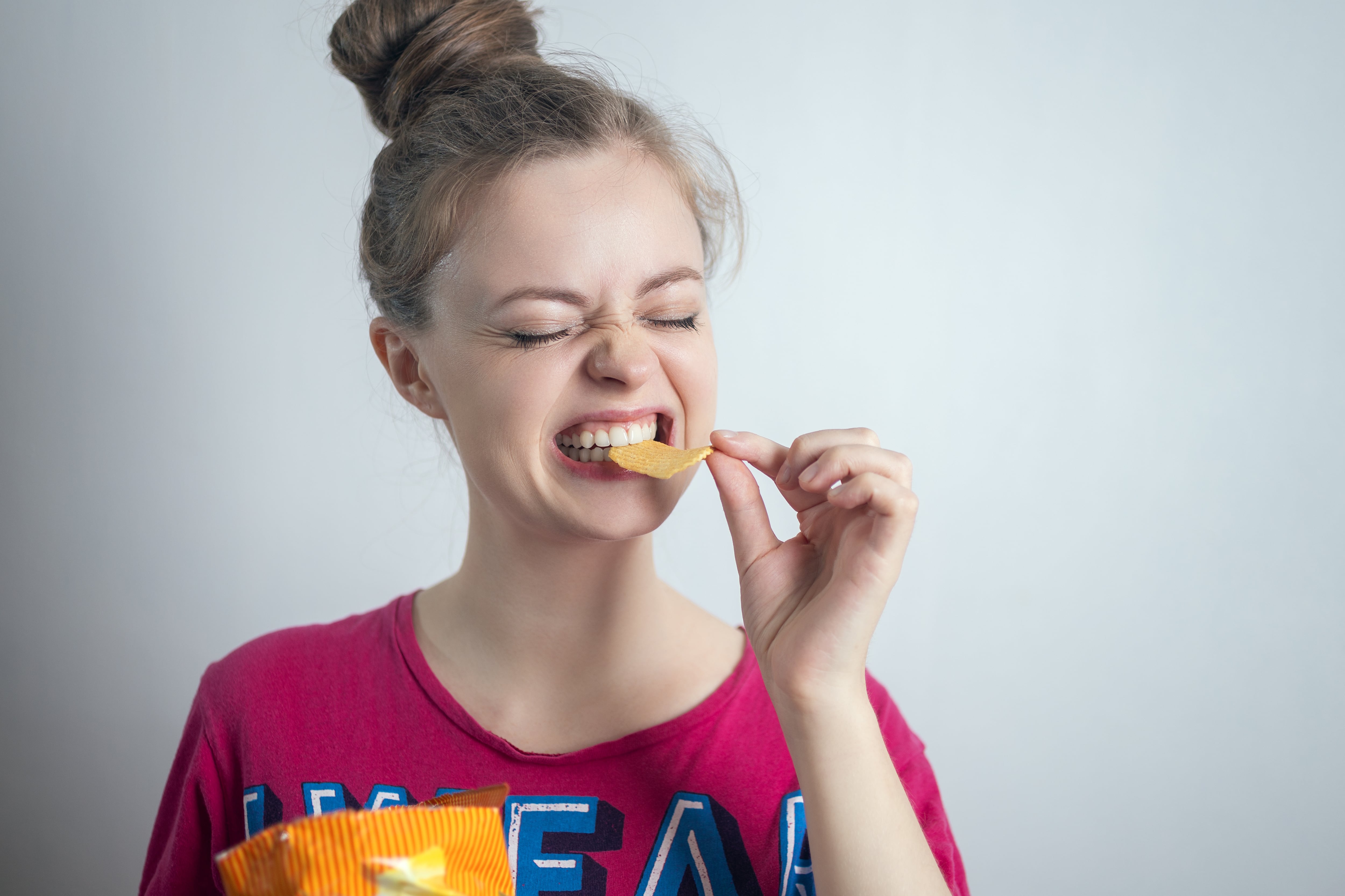 Smiling young Caucasian woman girl eating biting potato chips crisps aldarinho GettyImages