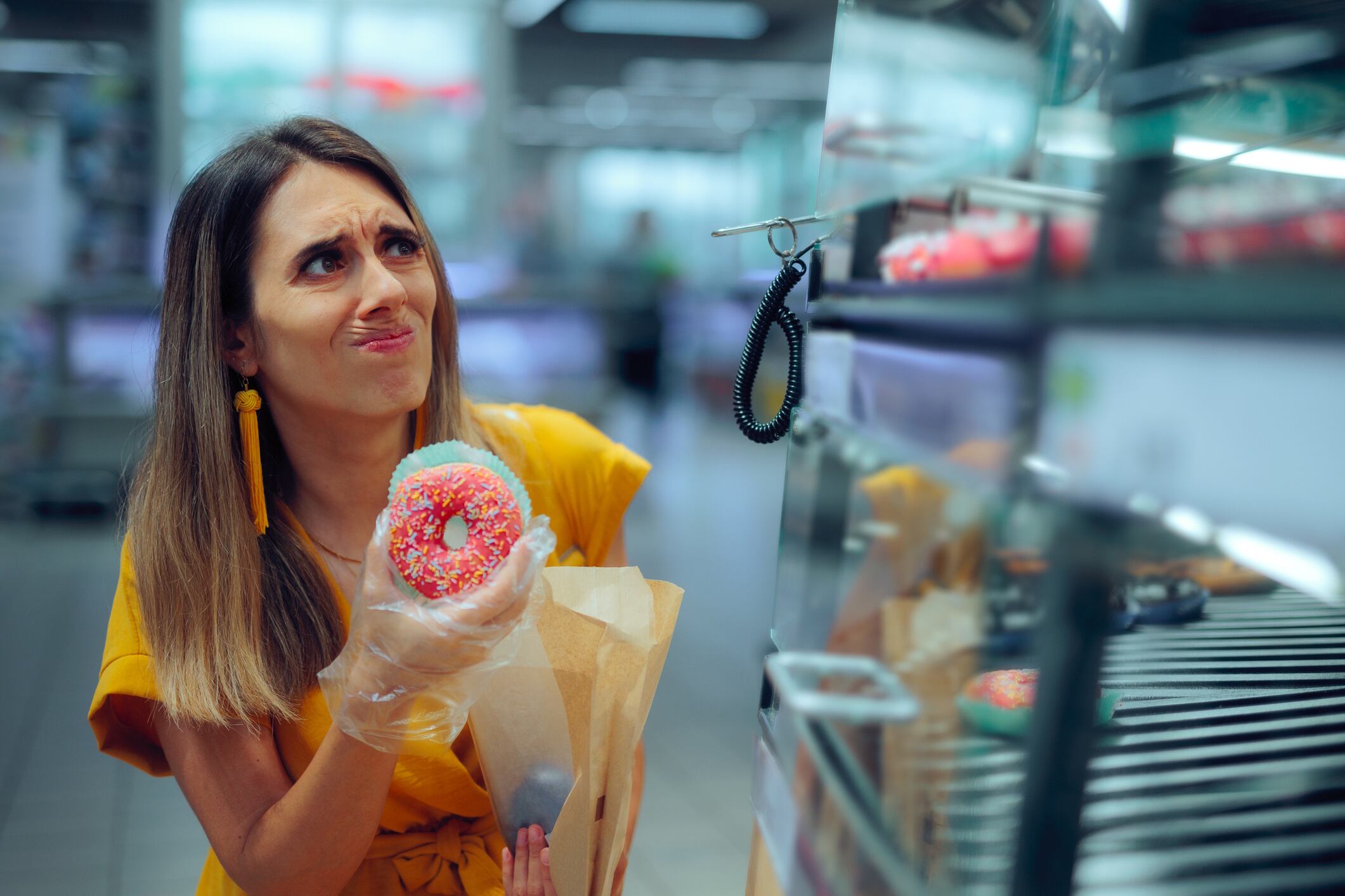 Uncertain Woman Taking a Doughnut with a Plastic Glove nicoletaionescu GettyImages