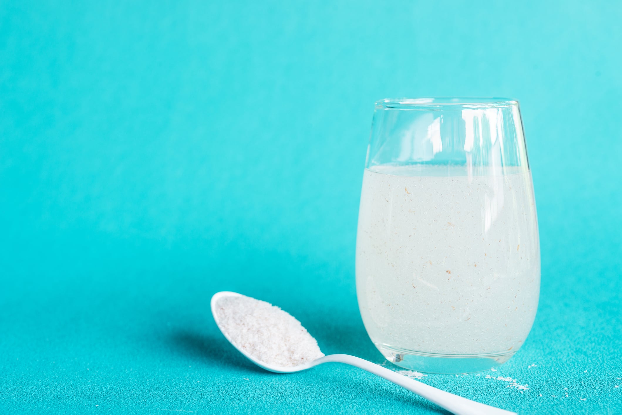 A glass of water soluble psyllium husk dietary fiber supplement on light aqua background.