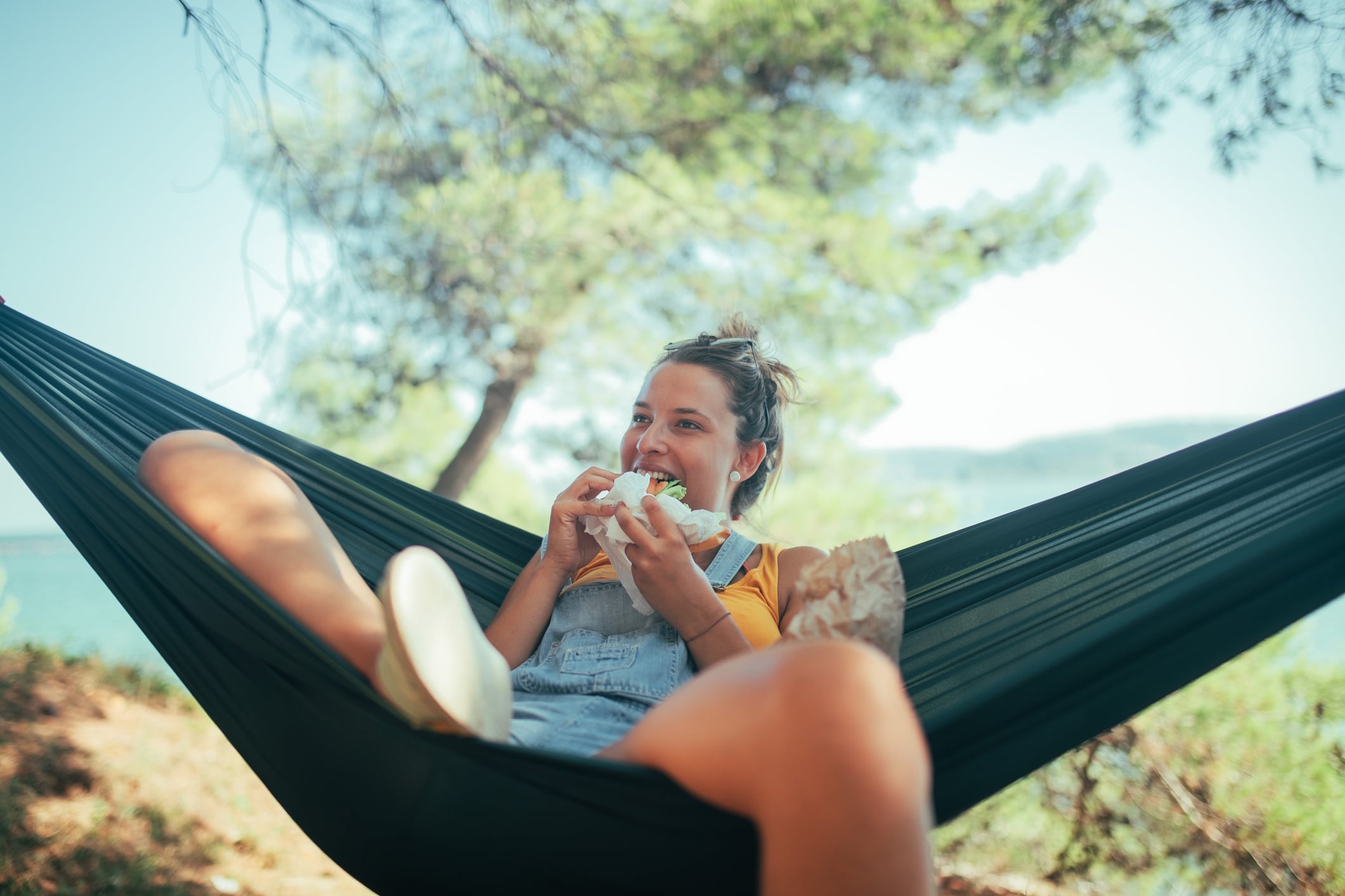 An image depicting a young woman enjoying her vacation. She's in remote woods, lying in a hammock and enjoying the surrounding. GettyImages-1342155769 Lajst