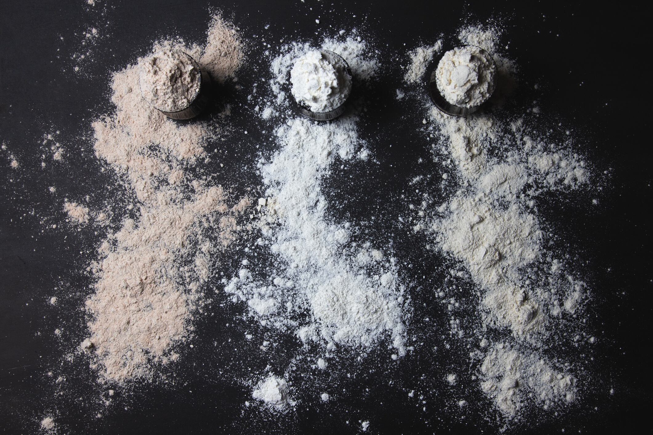 Three jars full of different types of flour, gluten free alternatives, sprinkled flour, black background Stely Nikolova GettyImages