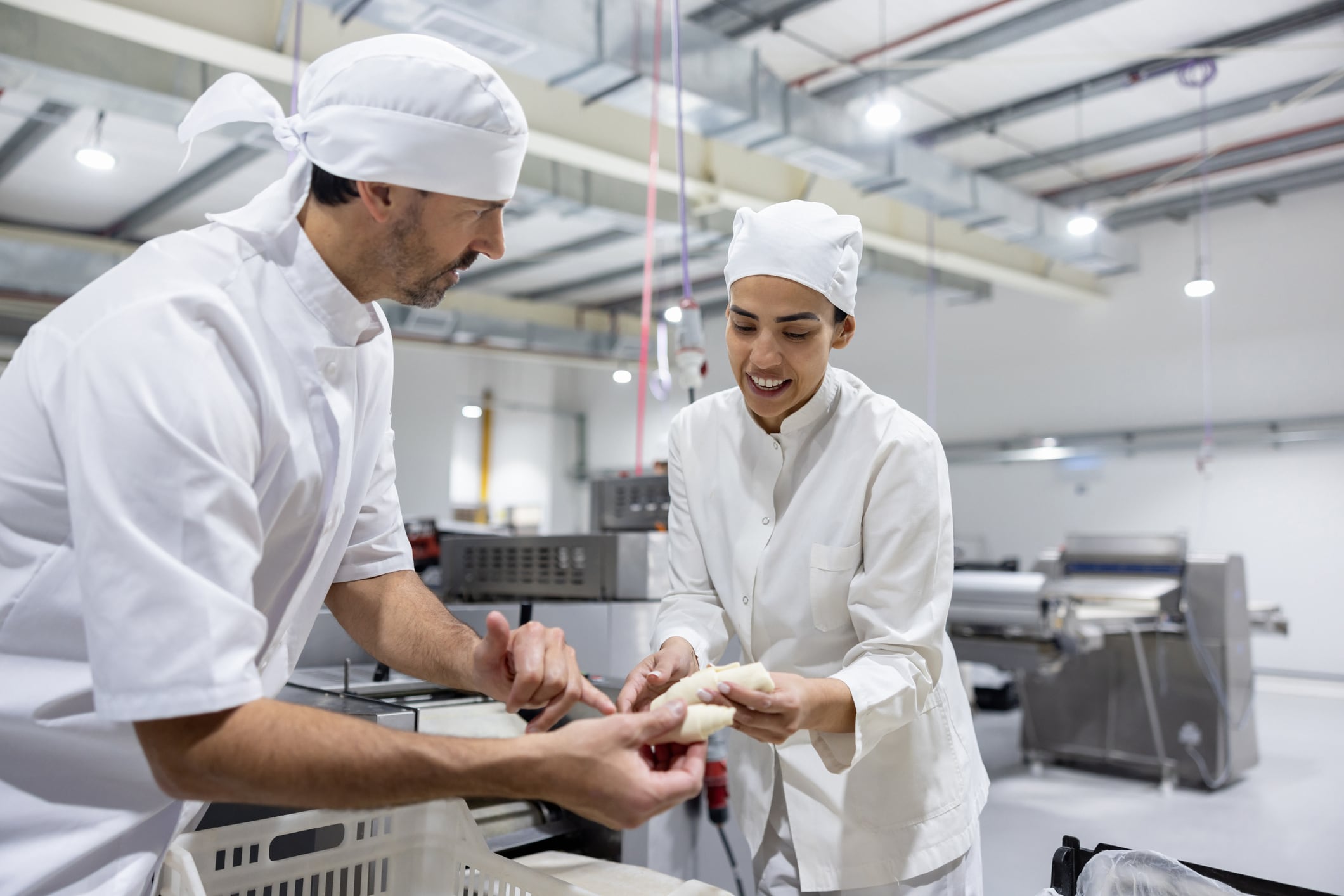 Latin American man training a new worker making croissants at an industrial bakery - food processing plant concepts