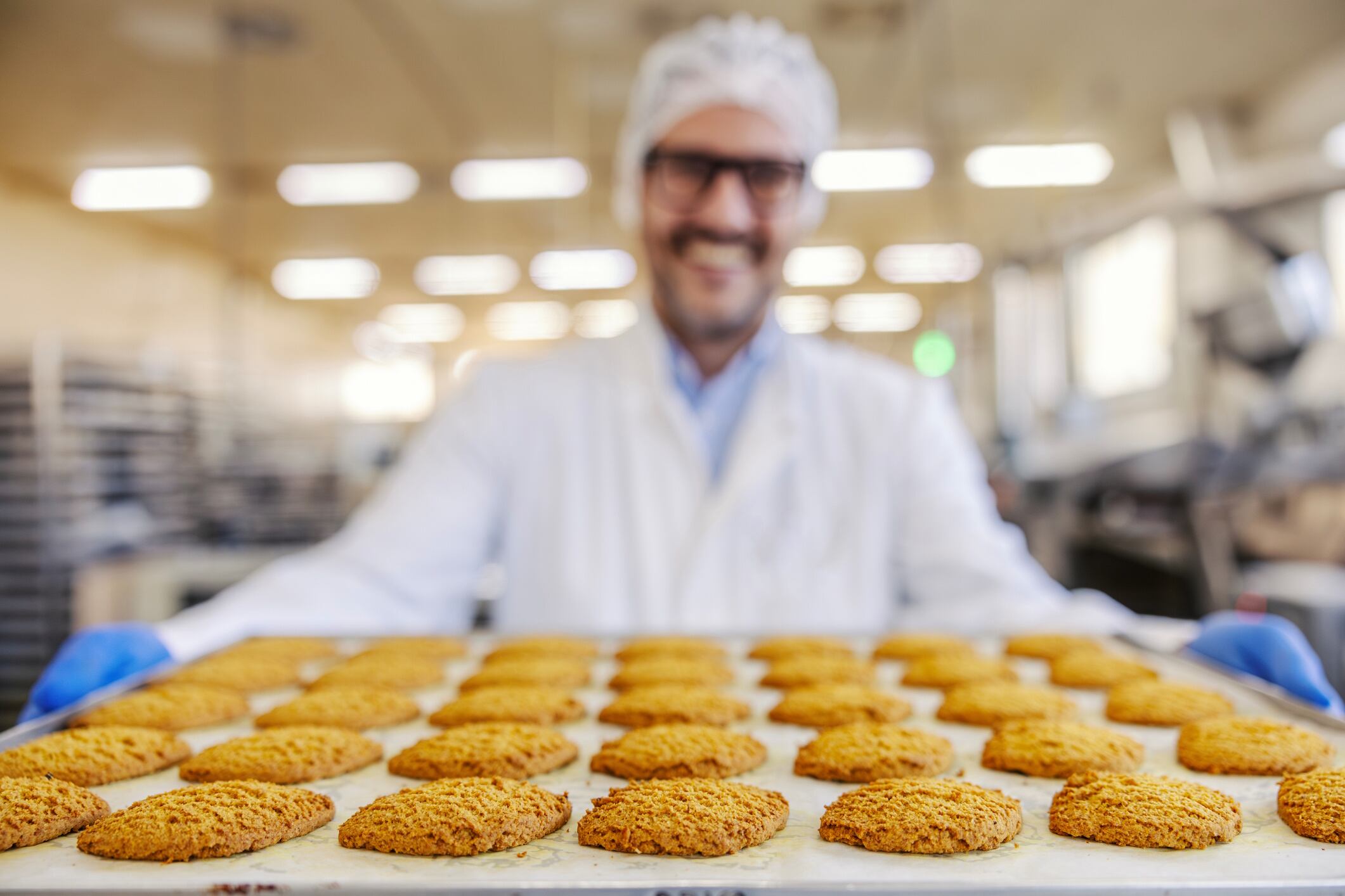 Worker holding tray of fresh baked oatmeal cookies in food factory