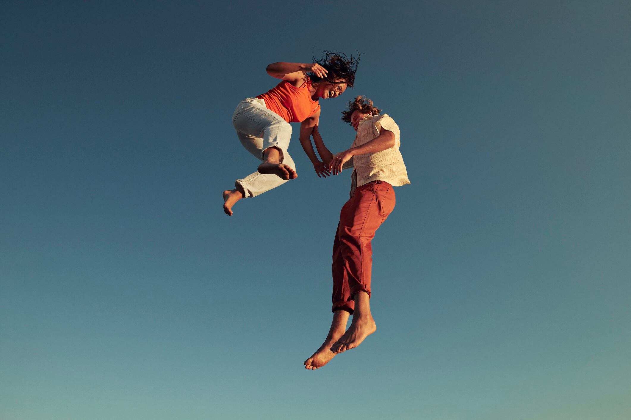 Low angle view of man and woman jumping high up into the air, against clear blue sky.