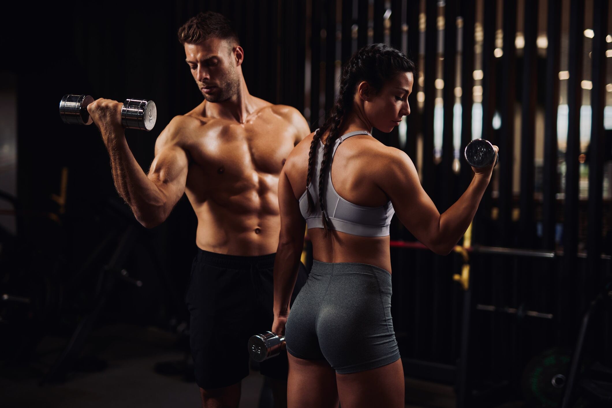 Young couple working out in the gym using dumbbells for bicep curls