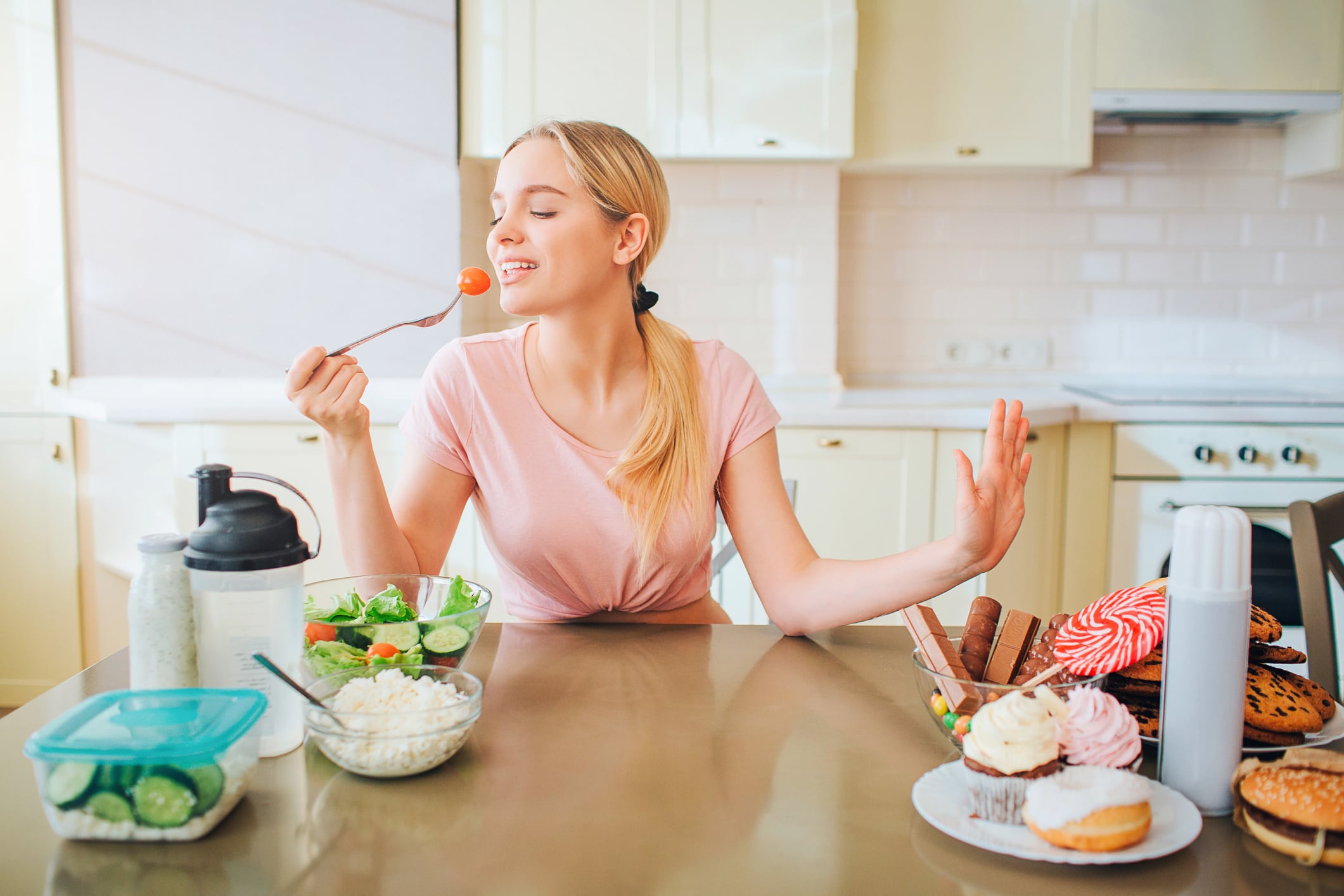 Nice young well-built model eting healthy food in kitchen at table. She says no to junk meal. Alone in kitchen. Daylight. Healthy lifestyle