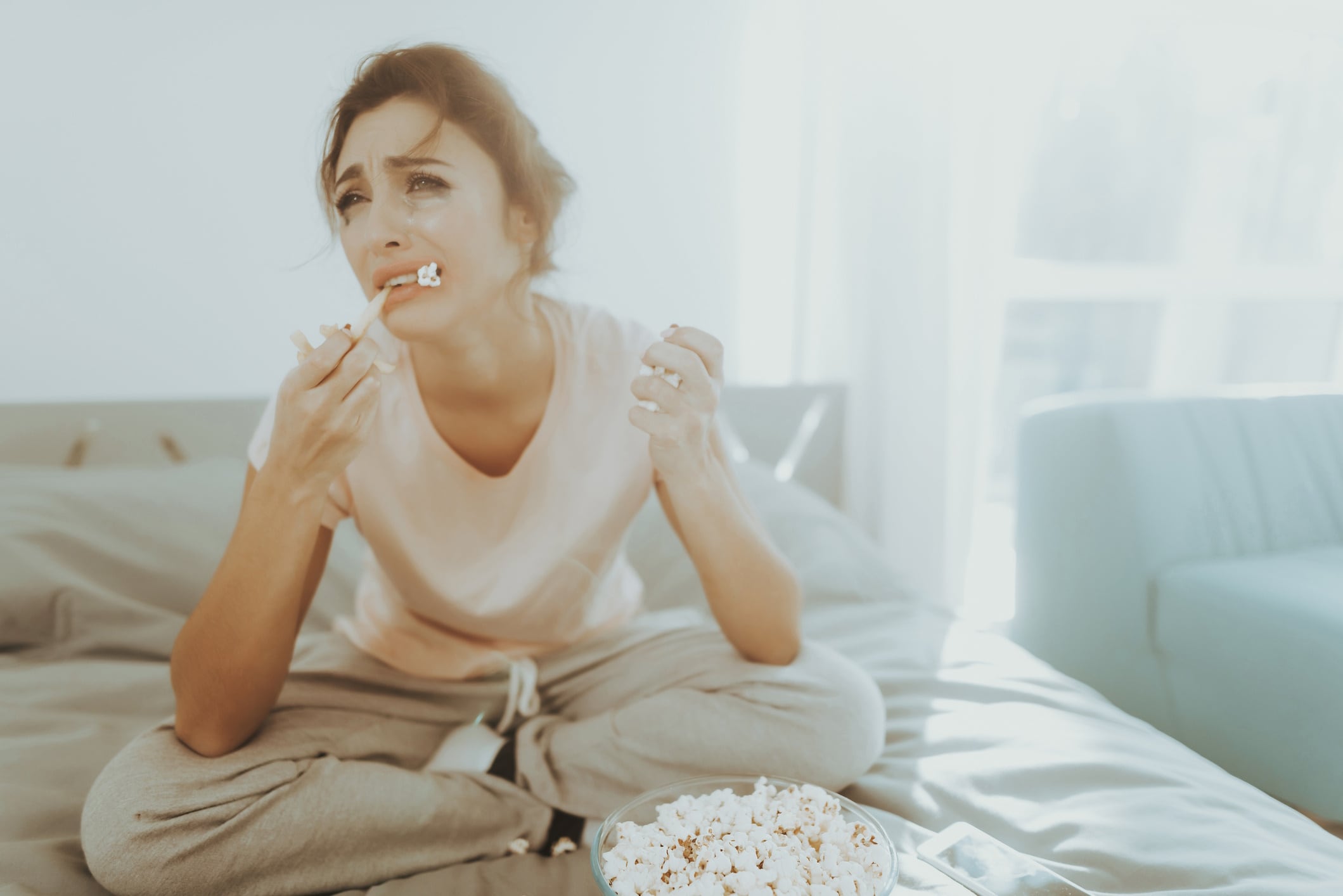 Unhappy woman eating popcorn on a bed