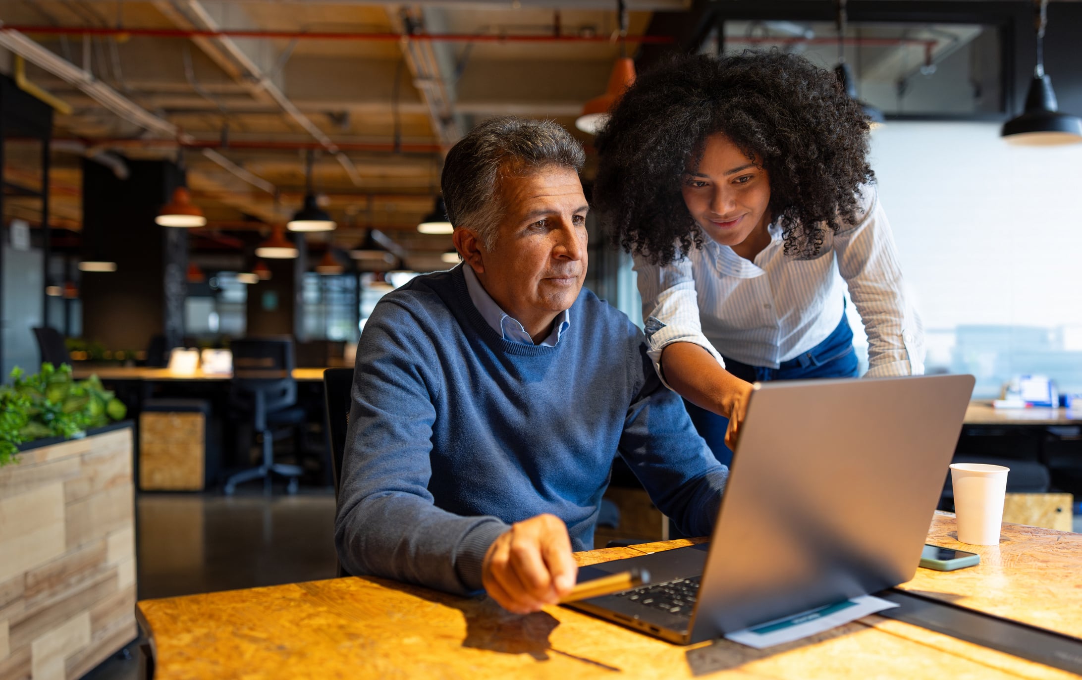 Gen Z businesswoman explaining something to a Gen X coworker on his laptop while working at the office