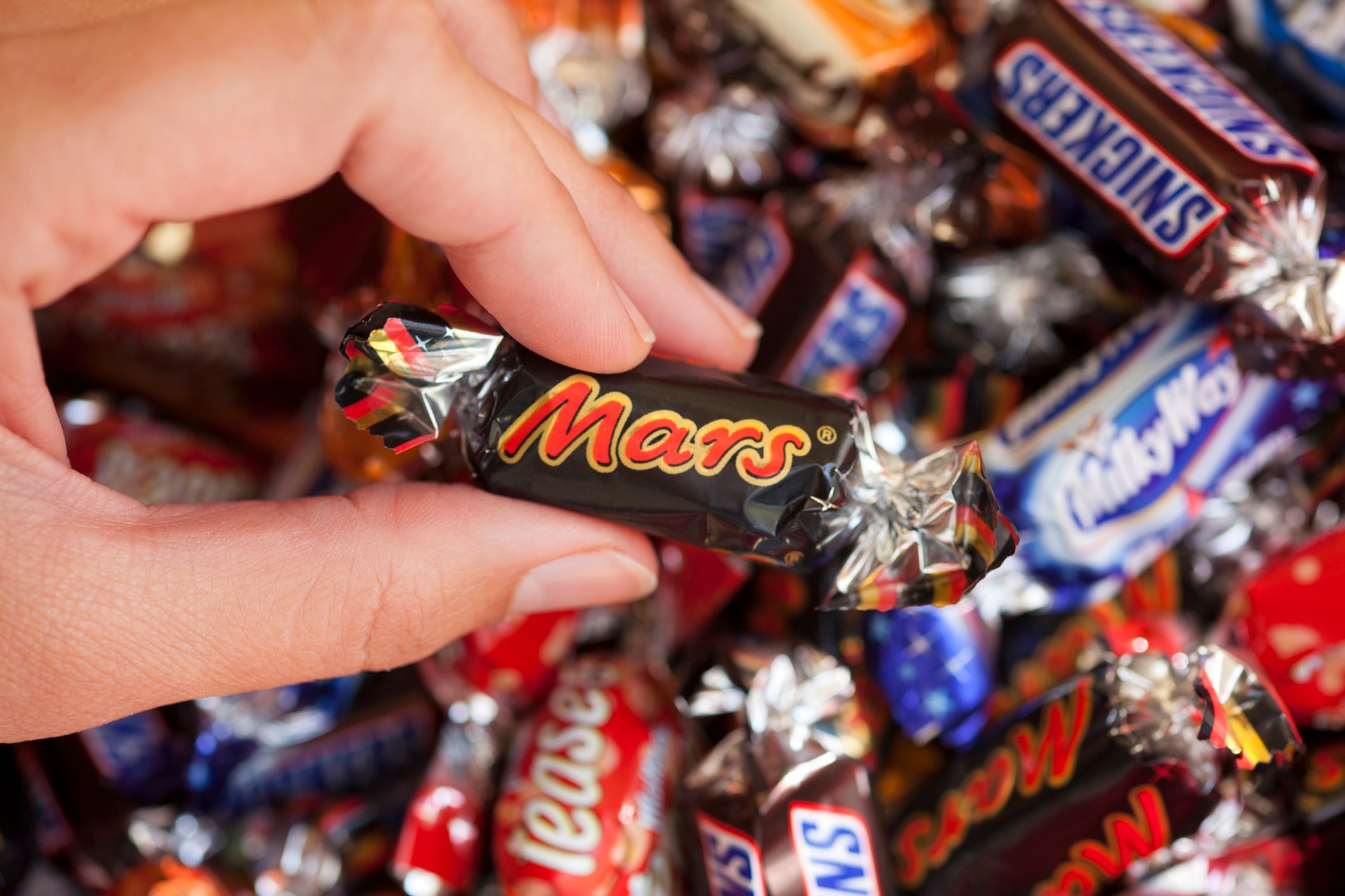 Woman's hand with background of Snickers, Mars, Twix, Milky Way, Galaxy, Bounty and Maltesers.