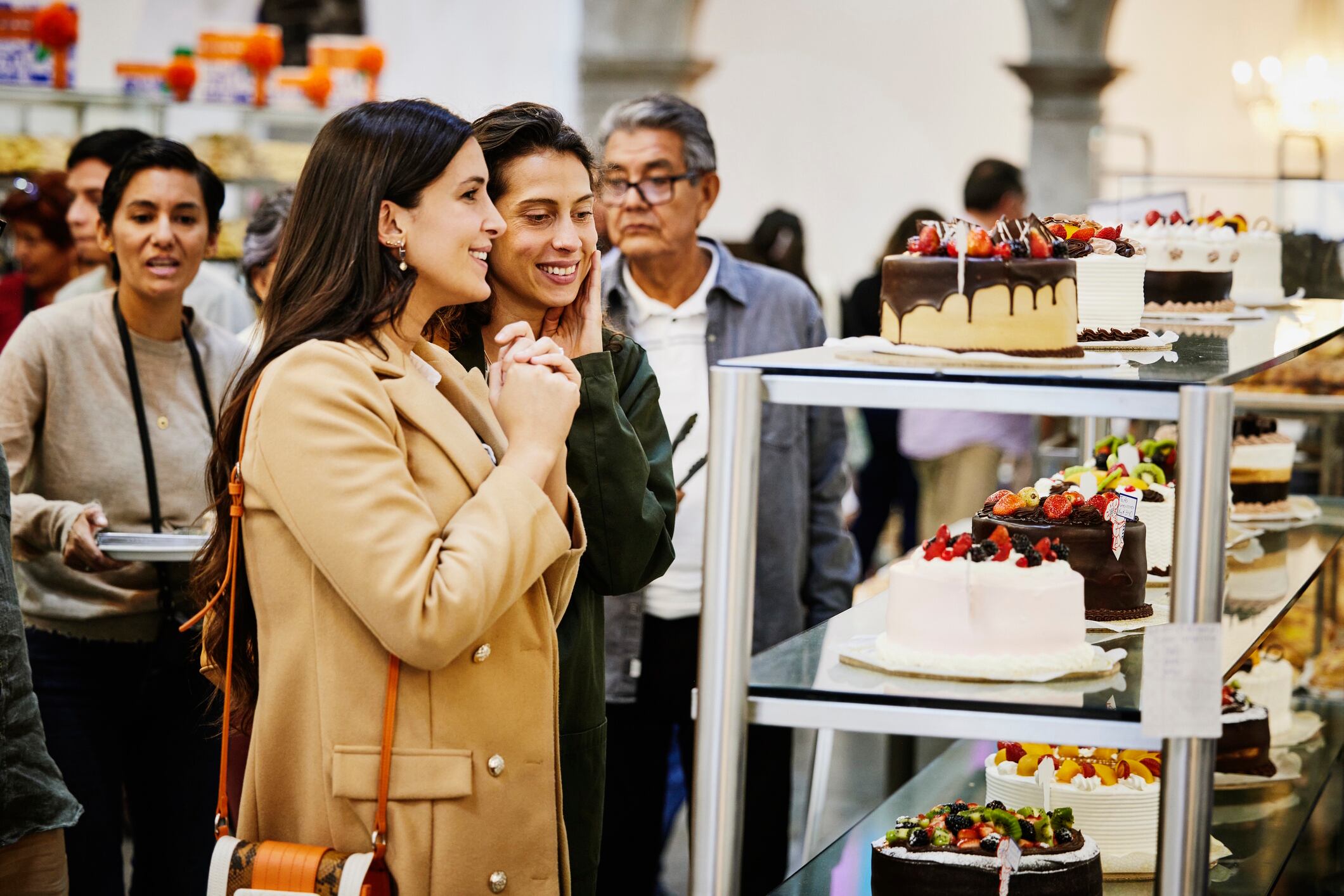 Medium wide shot smiling friends admiring cakes while visiting bakery Thomas Barwick GettyImages