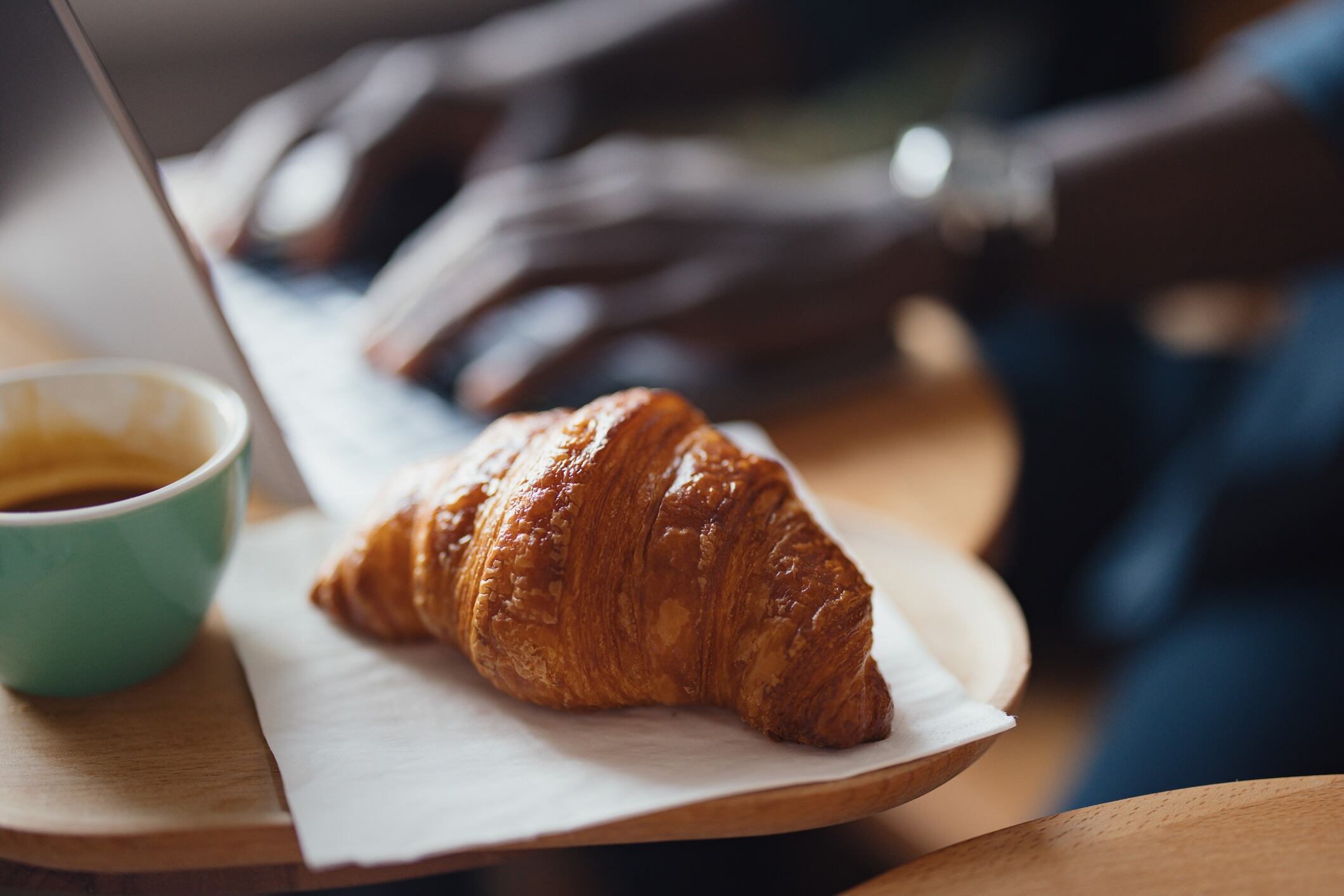 Close up of person on a laptop with croissant and coffee in foreground
