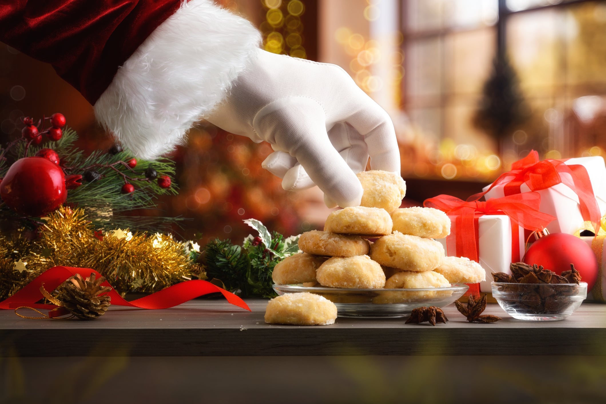 Santa's hand taking cookie on table with Christmas decorations
