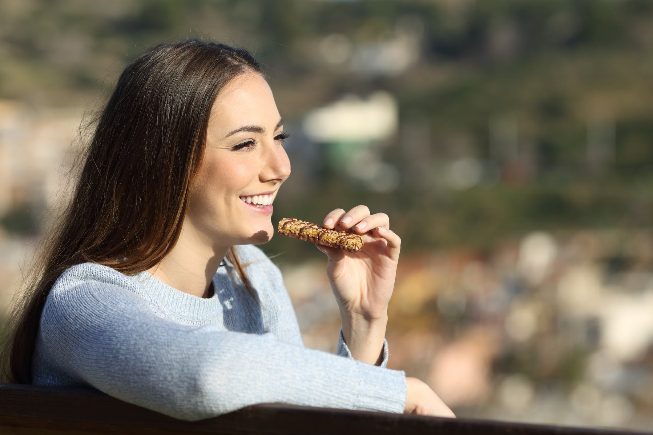 Woman eating snack bar on park bench