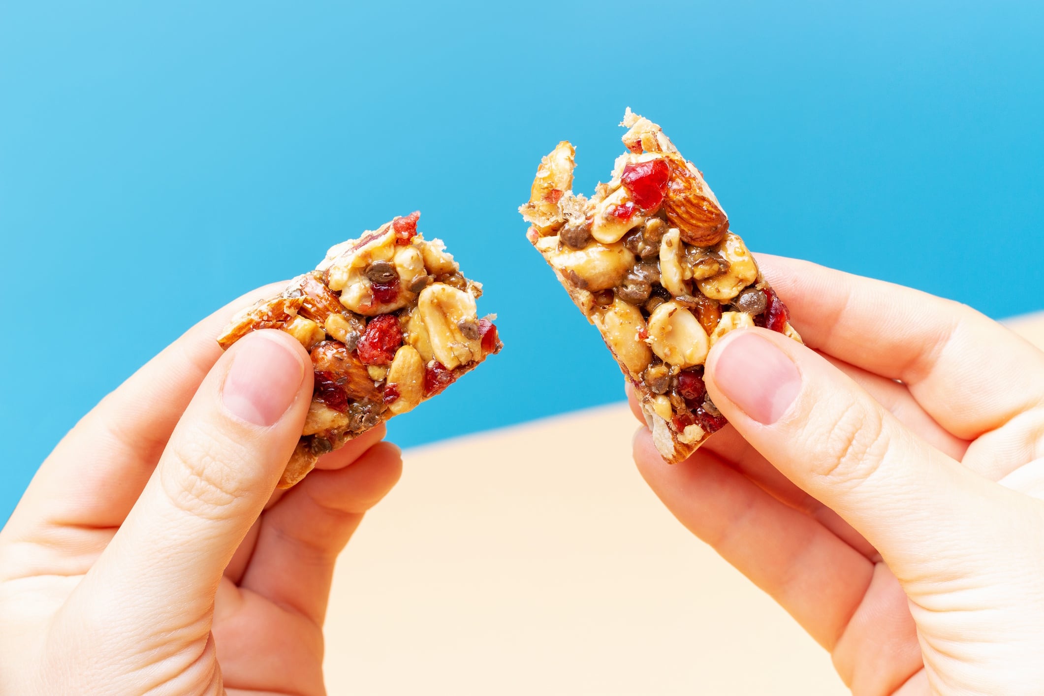 Female hands holding broken piece of protein bar on blue and brown background Tatiana GettyImages