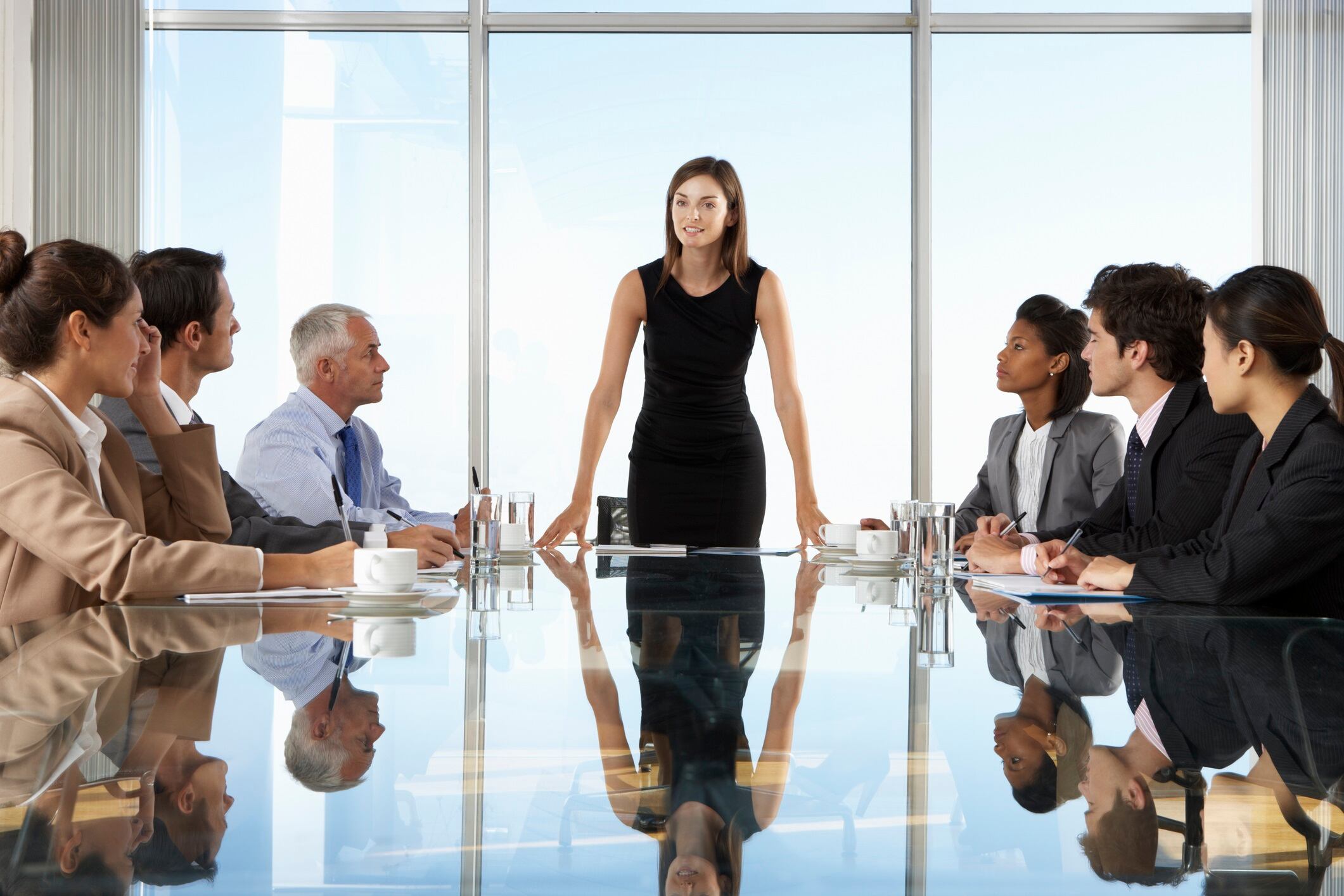 Woman hosting board meeting around glass table.