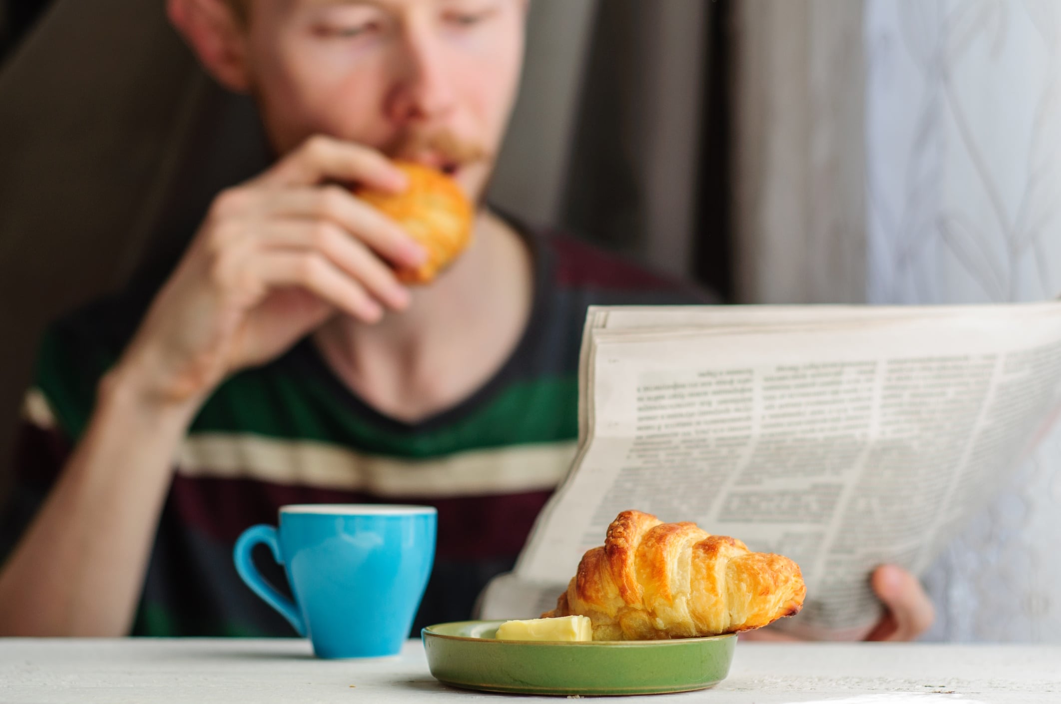 Man reading newspaper while eating croissant