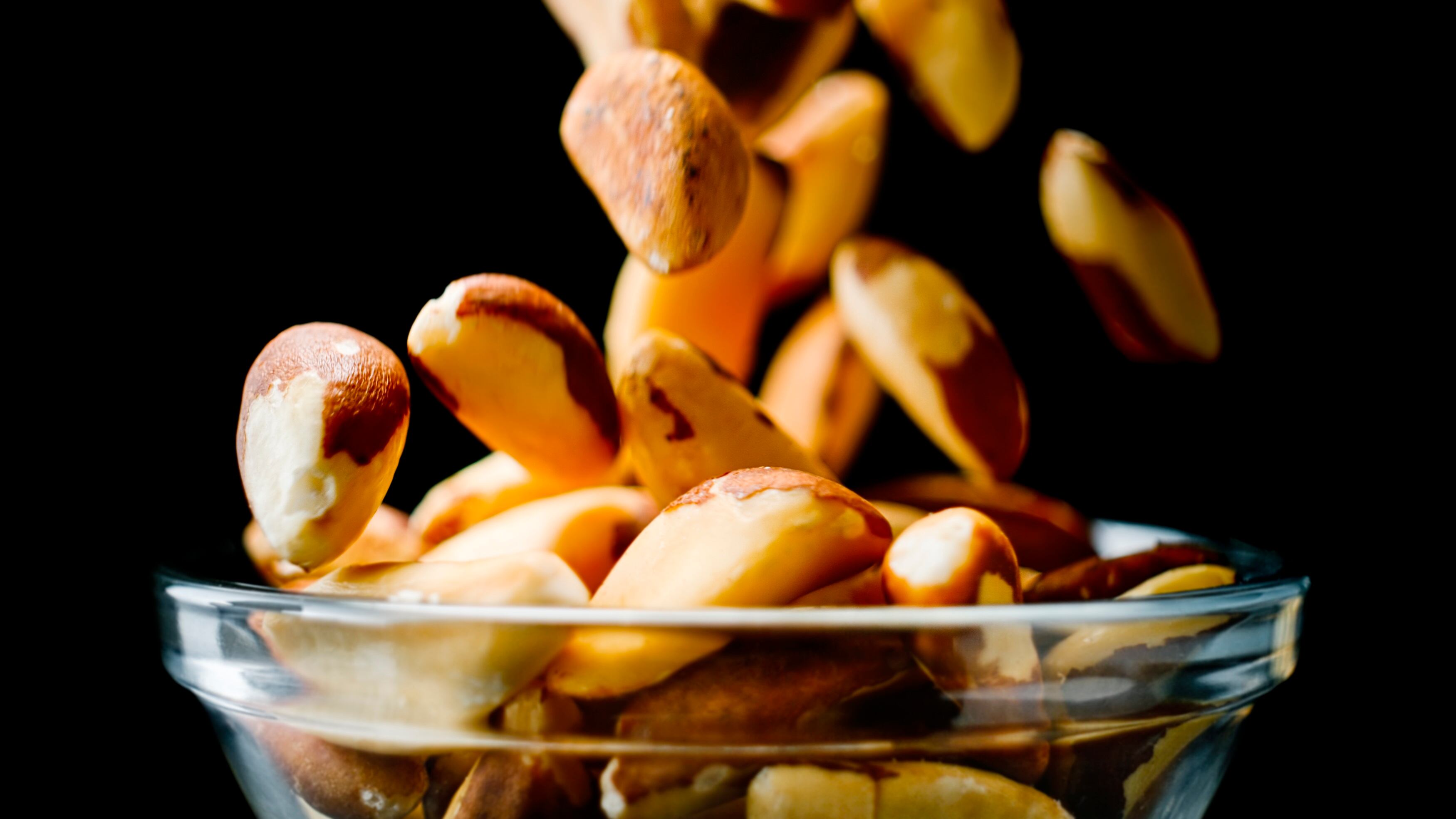 Close up of Brazil nuts into a glass bowl against black background.