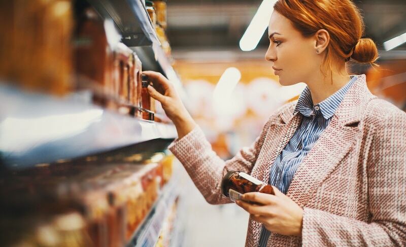 Woman examines jar of sun-dried tomatoes at store